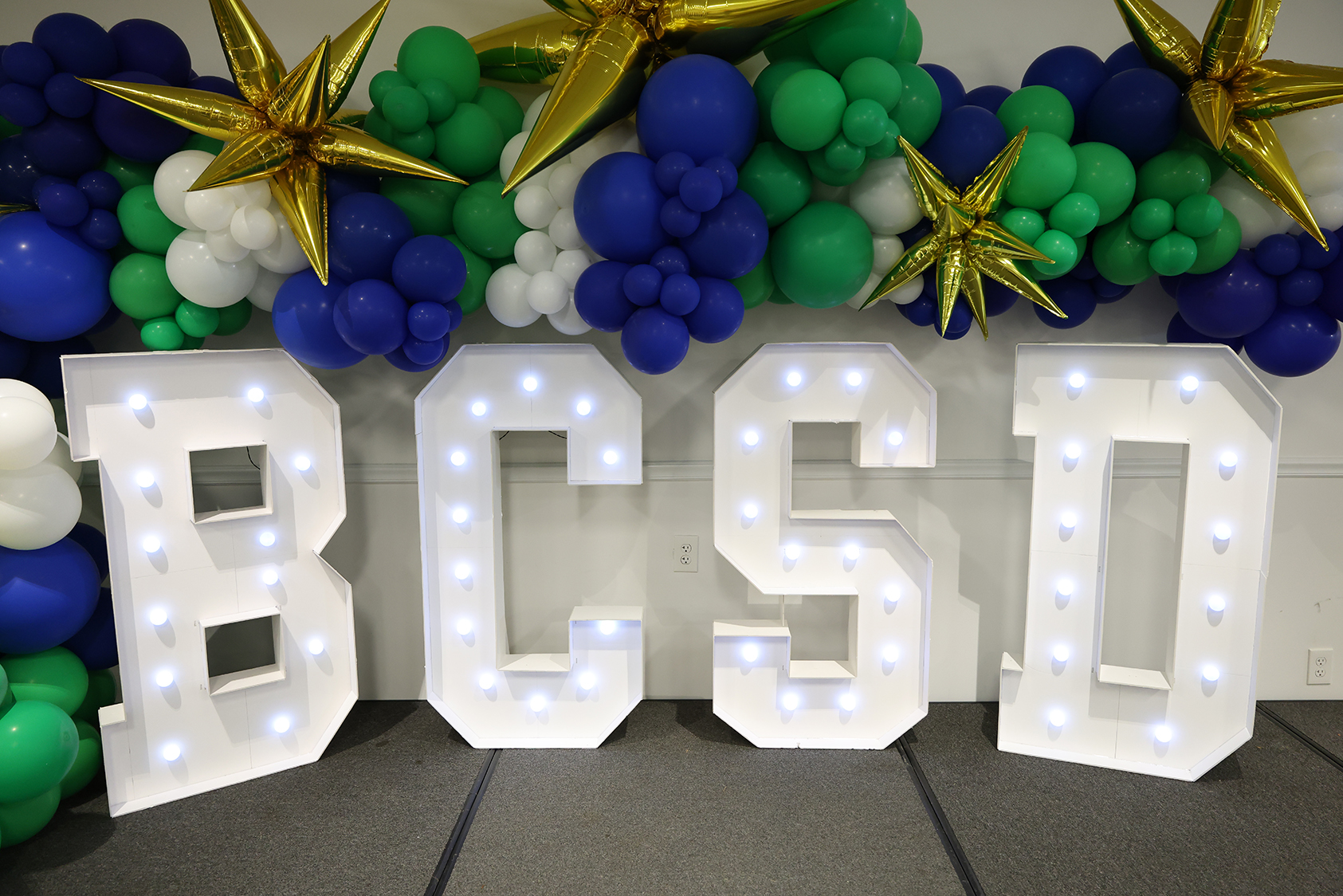 A large white display spells "BCSD" with blue lights, set in front of a backdrop of colorful balloons.