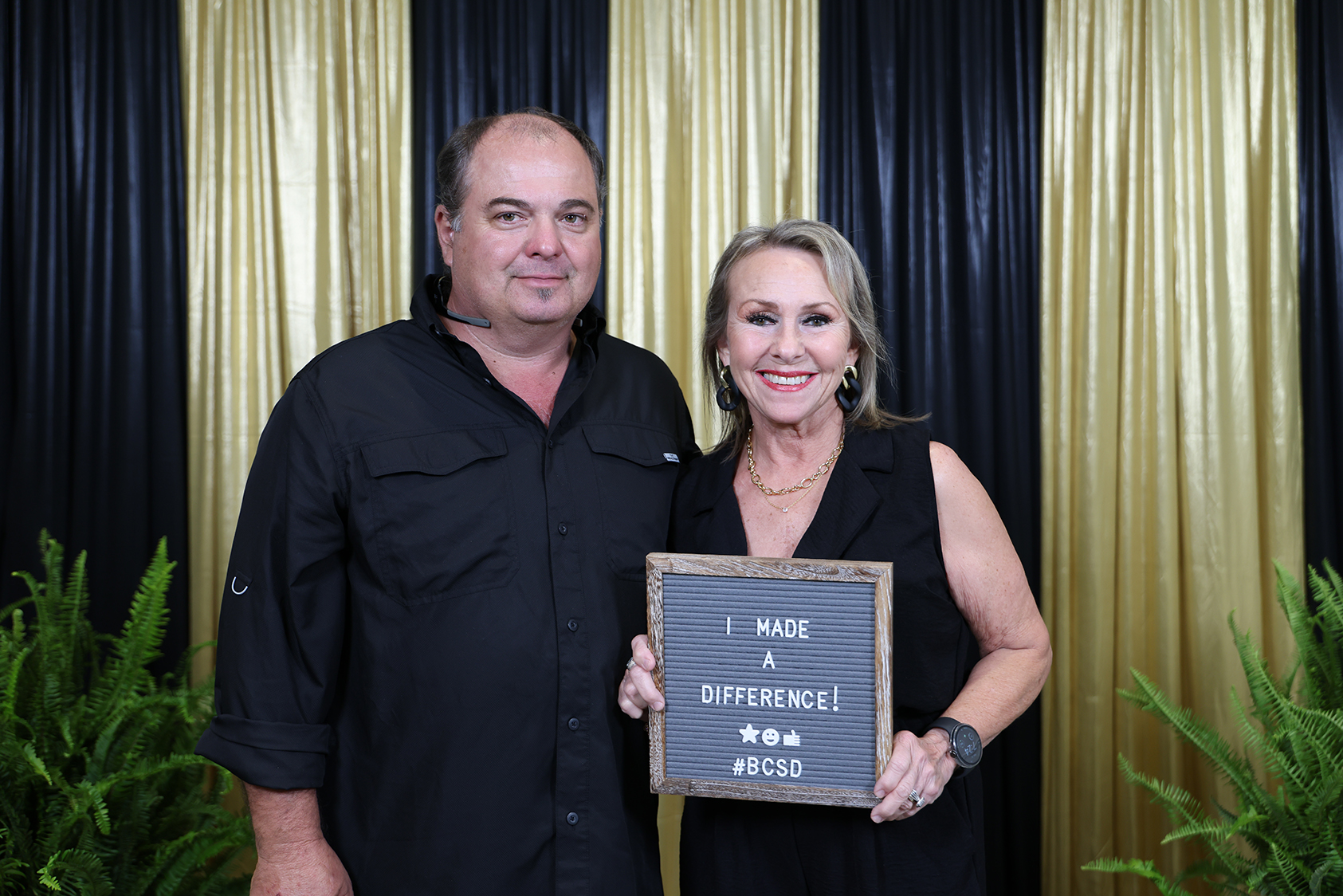 Man and woman standing next to each other. Woman holds a sign that reads "I MADE A DIFFERENCE".