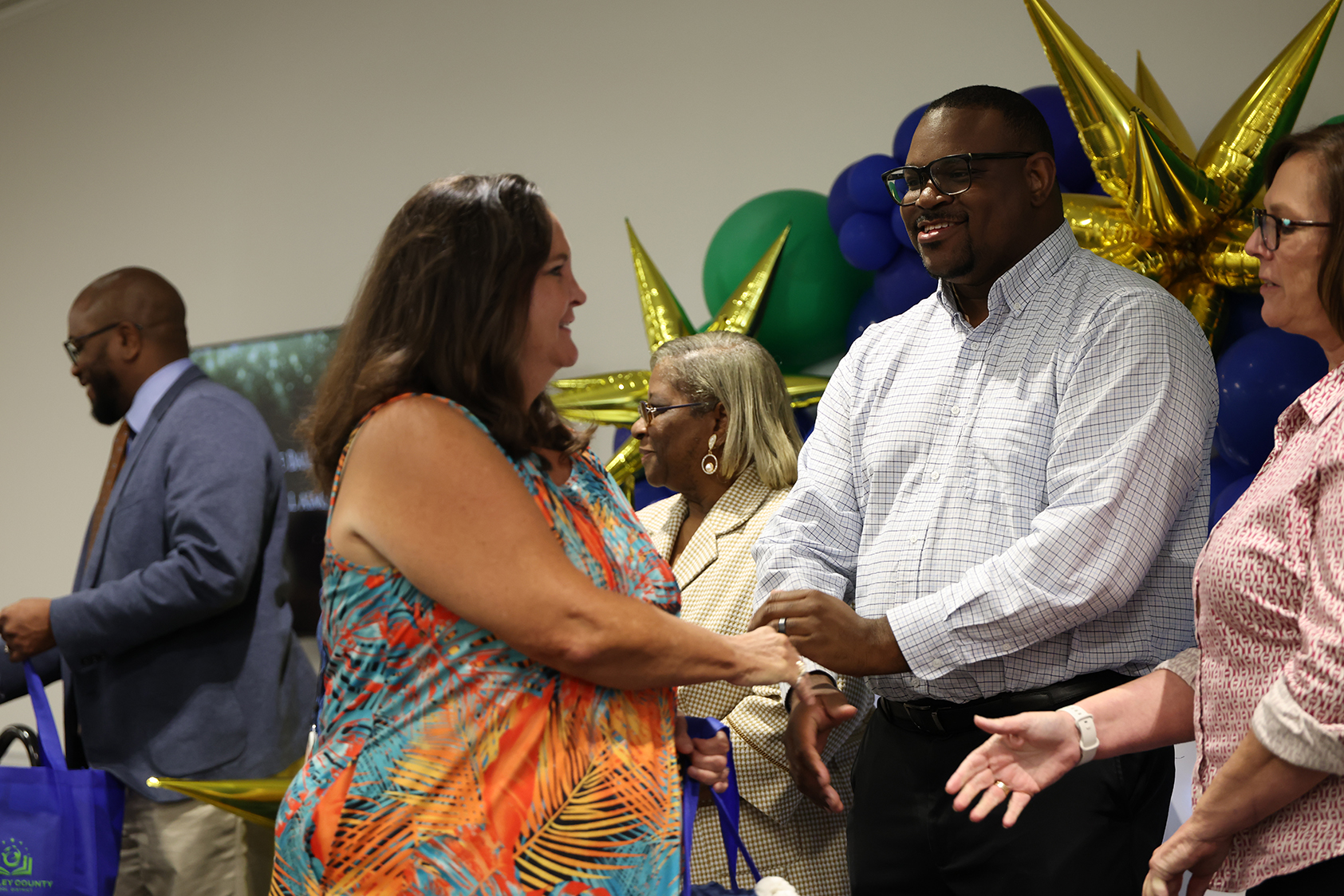 Five adults standing together. One man and one woman shake hands in the center.