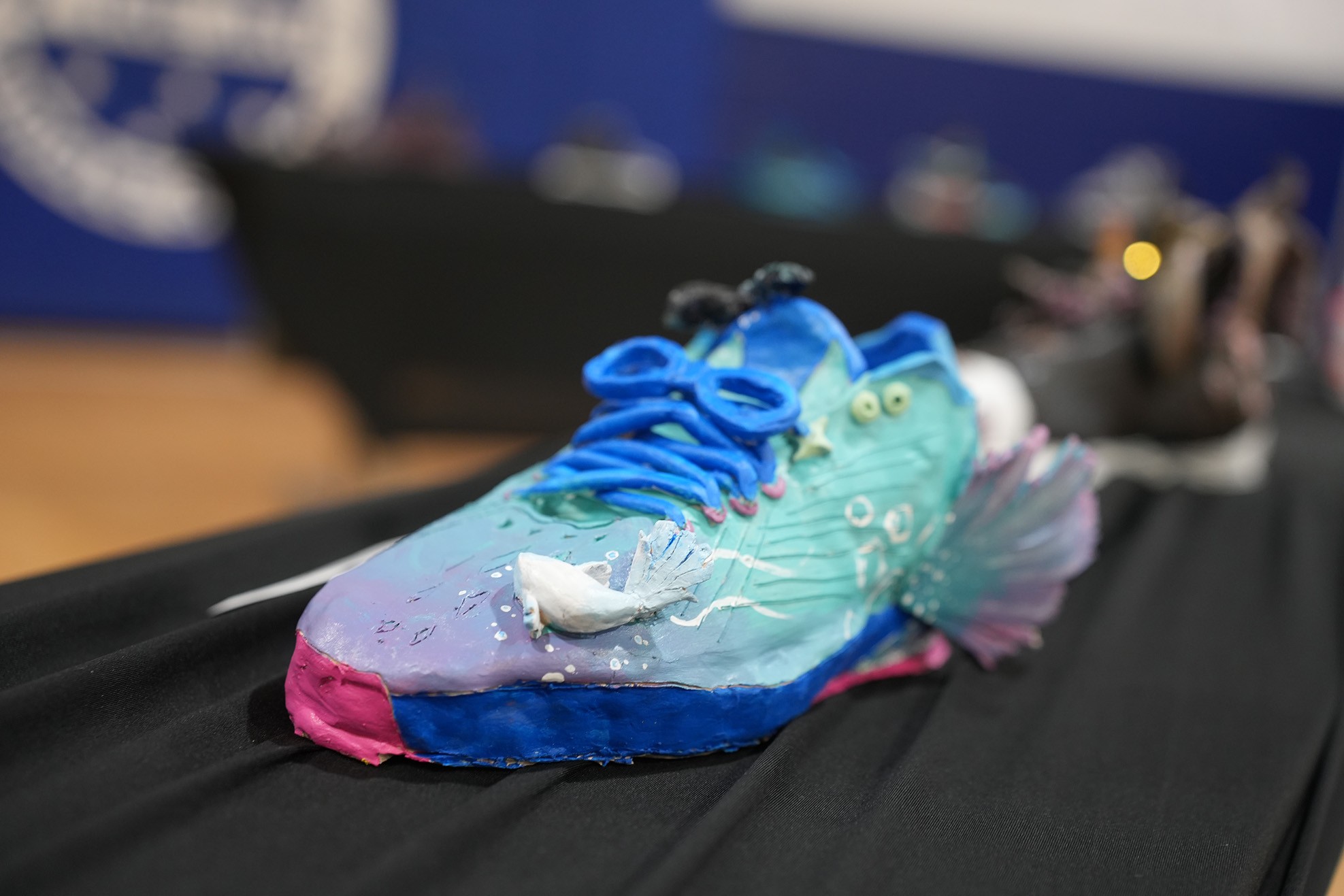 A custom-painted shoe, blue, green, and pink with a fish design, displayed on a black surface.