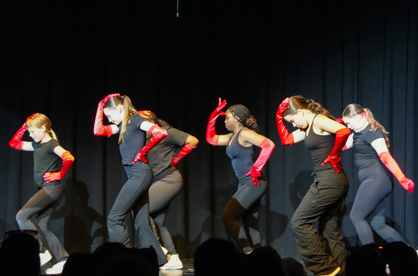 Five dancers wearing red gloves and dark clothing perform a synchronized dance routine on a stage.