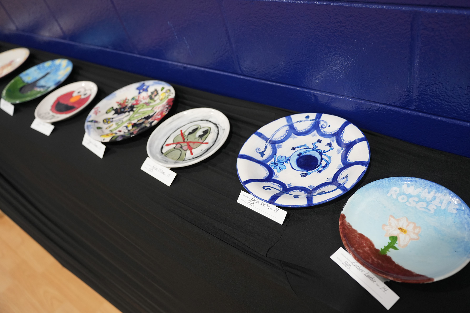 Multiple plates with unique designs displayed on a black table against a blue wall.
