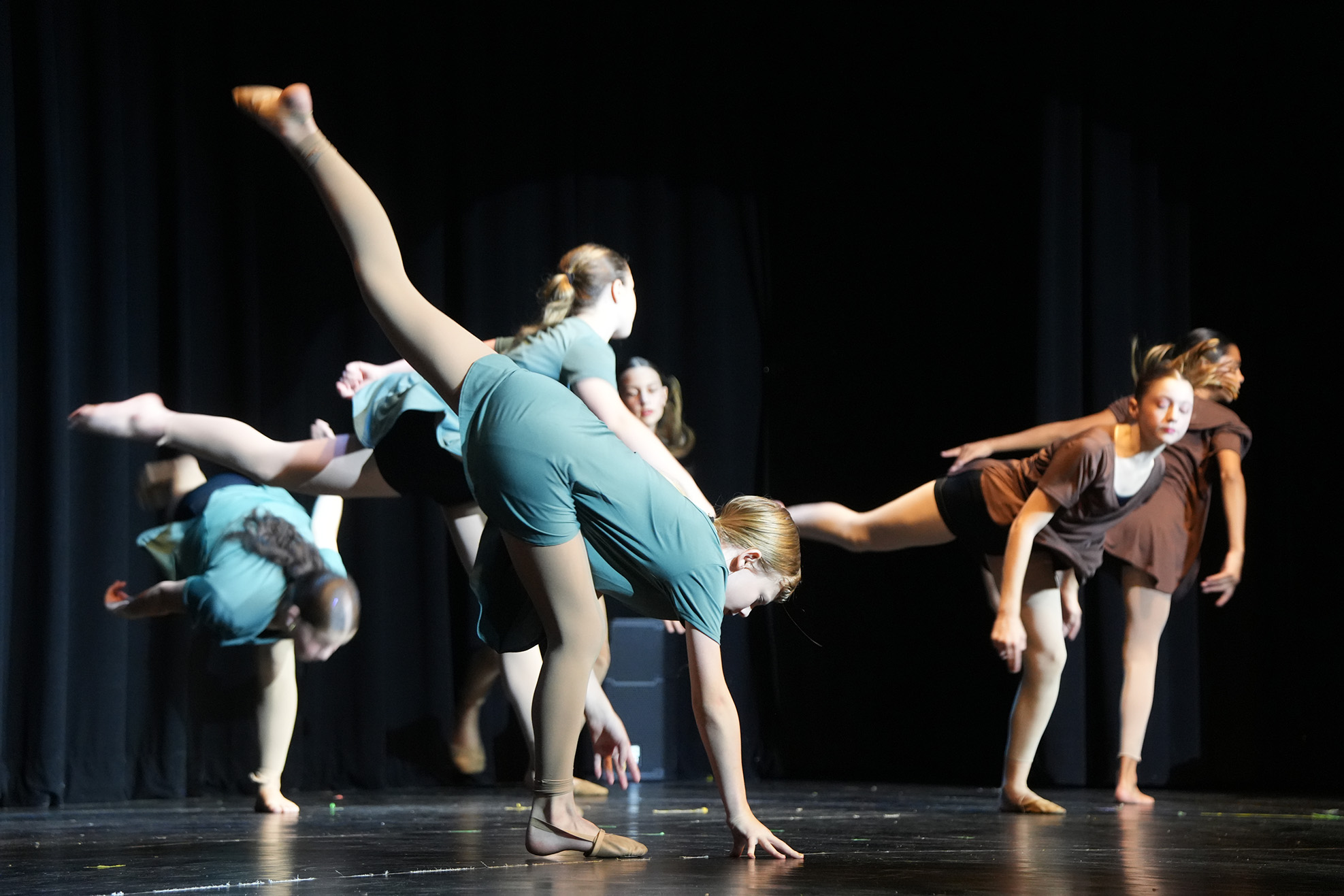 A group of women in blue and brown outfits perform a dance routine on a stage.