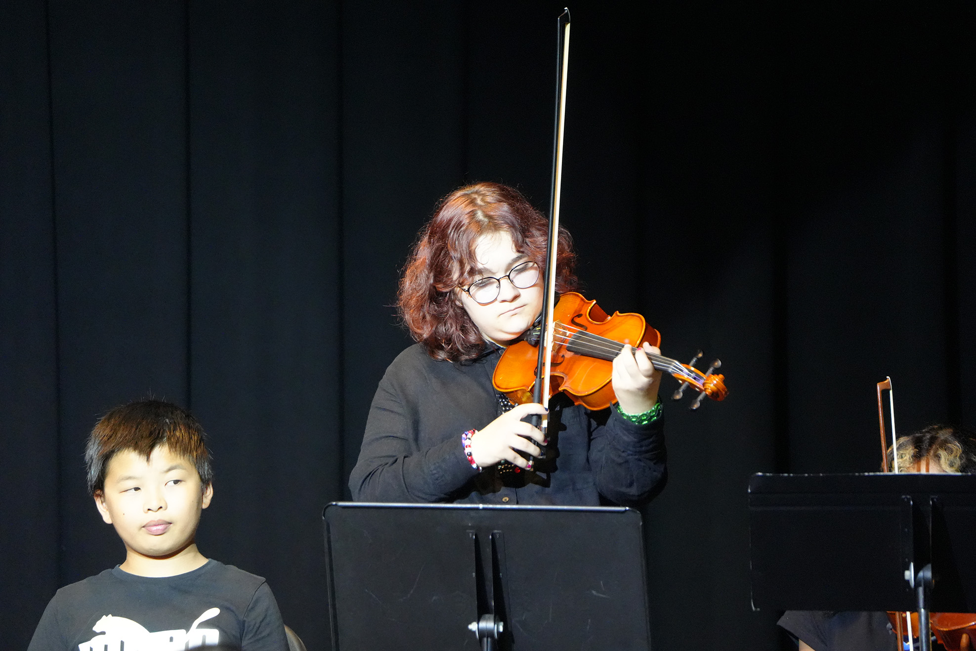 A violinist with curly hair holds an instrument, standing before a dark background. A child gazes at the violinist.