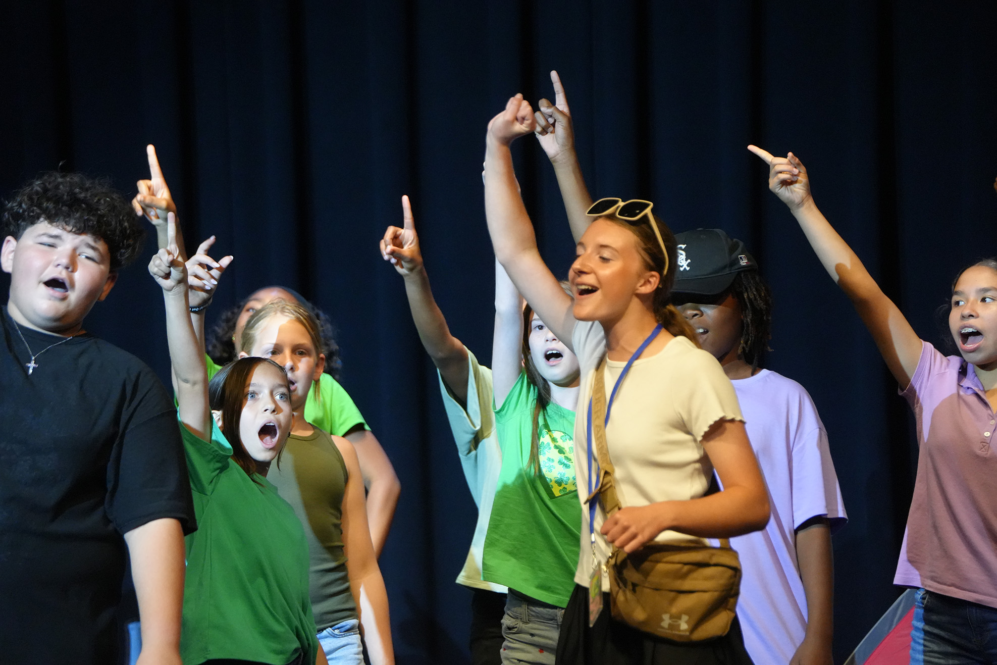A group of young people performing on a stage. They are wearing different colored shirts.