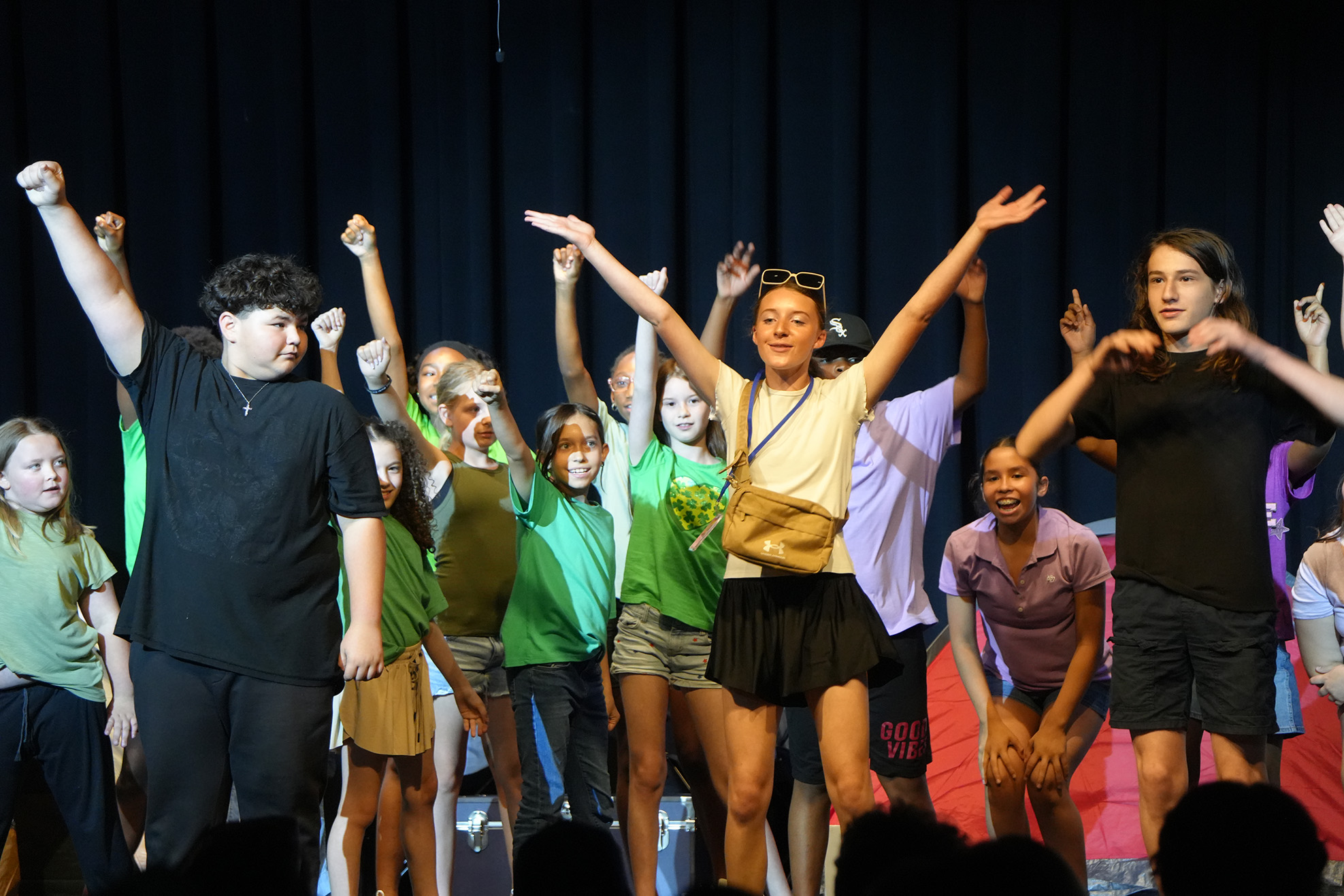 A group of young people, dressed in casual clothes, performing on stage with raised hands.