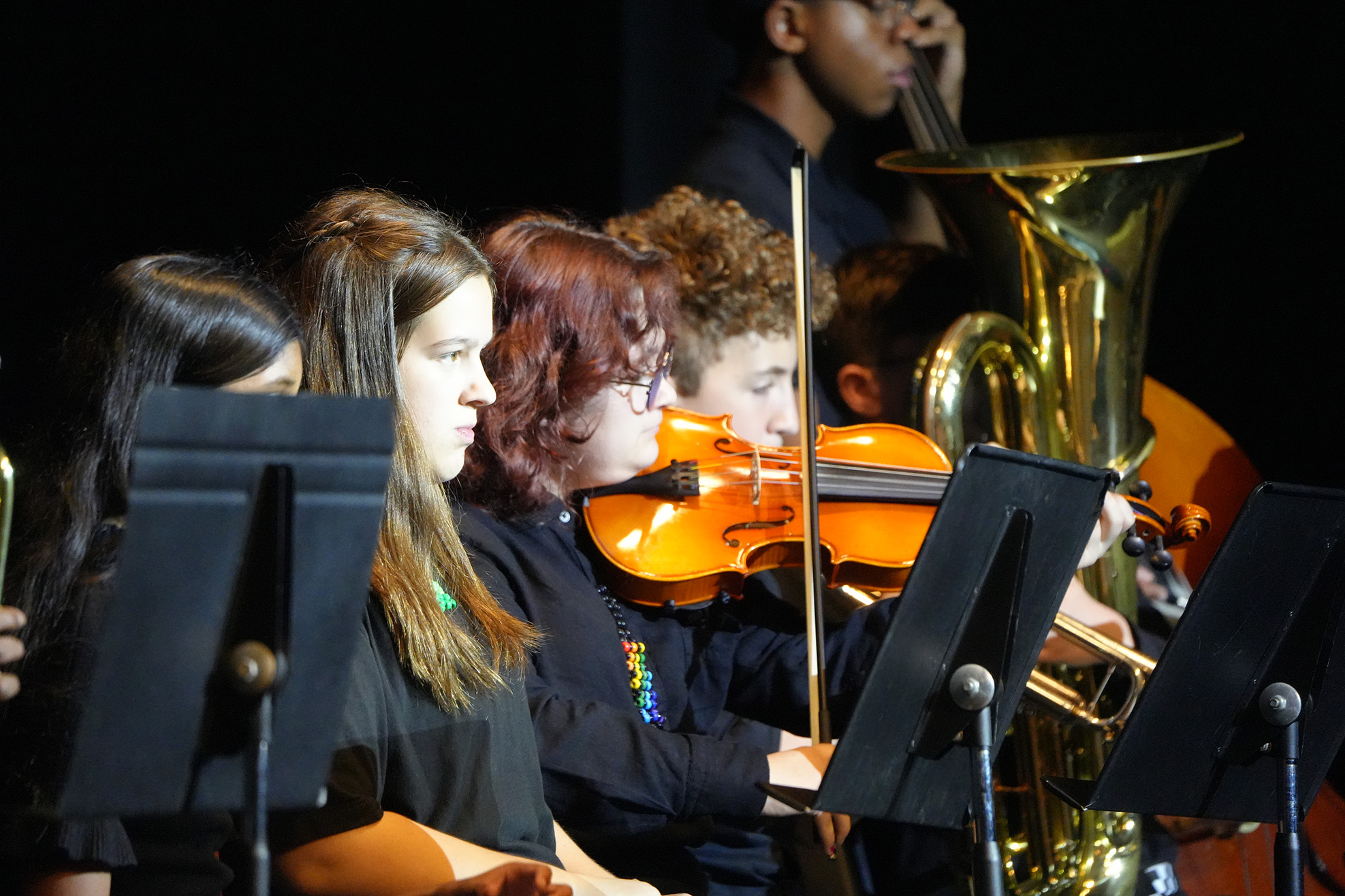 A group of children performs in a musical ensemble, playing instruments such as violin, cello, and tuba.