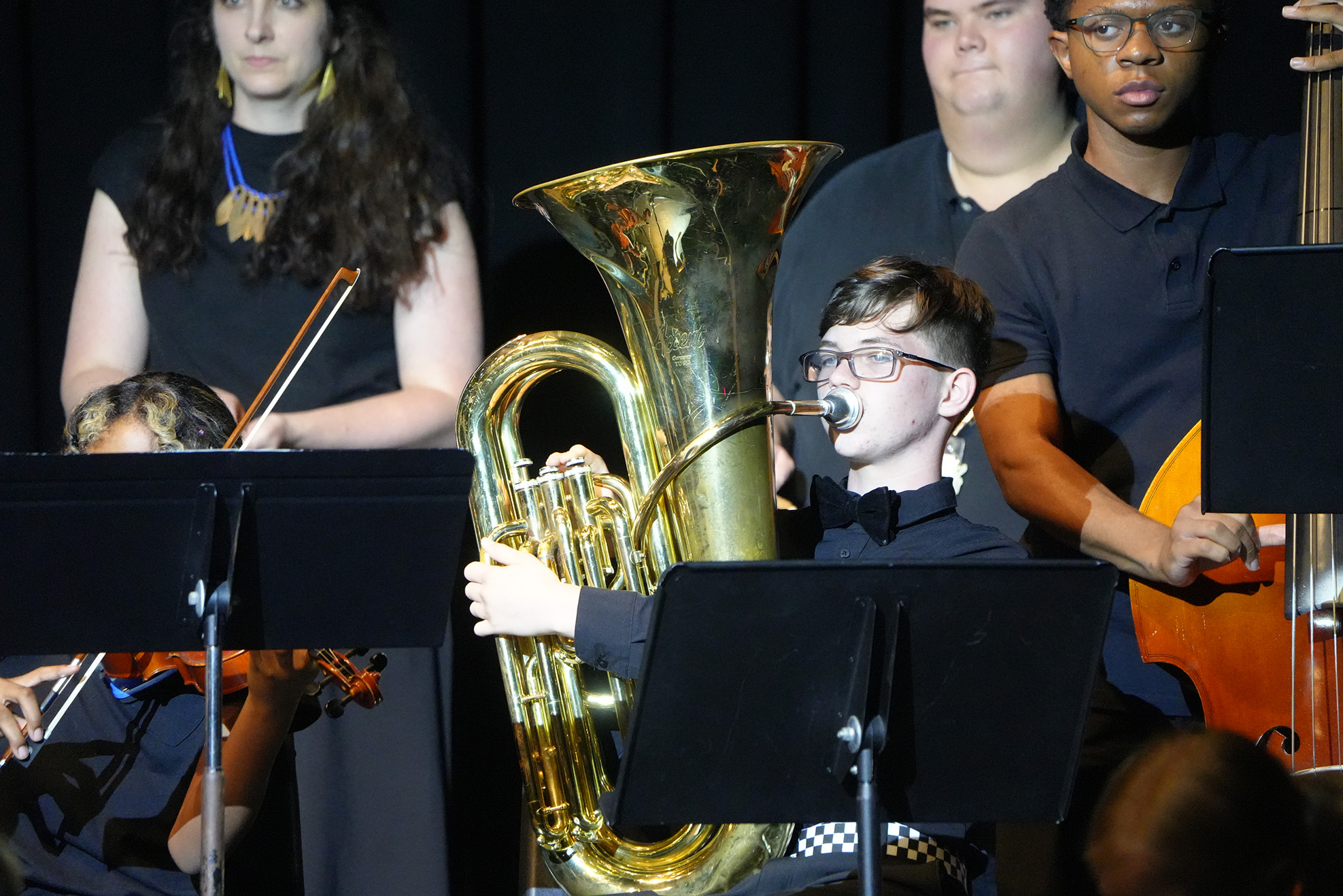 A group of musicians on stage, including a person playing a tuba and others playing violin.