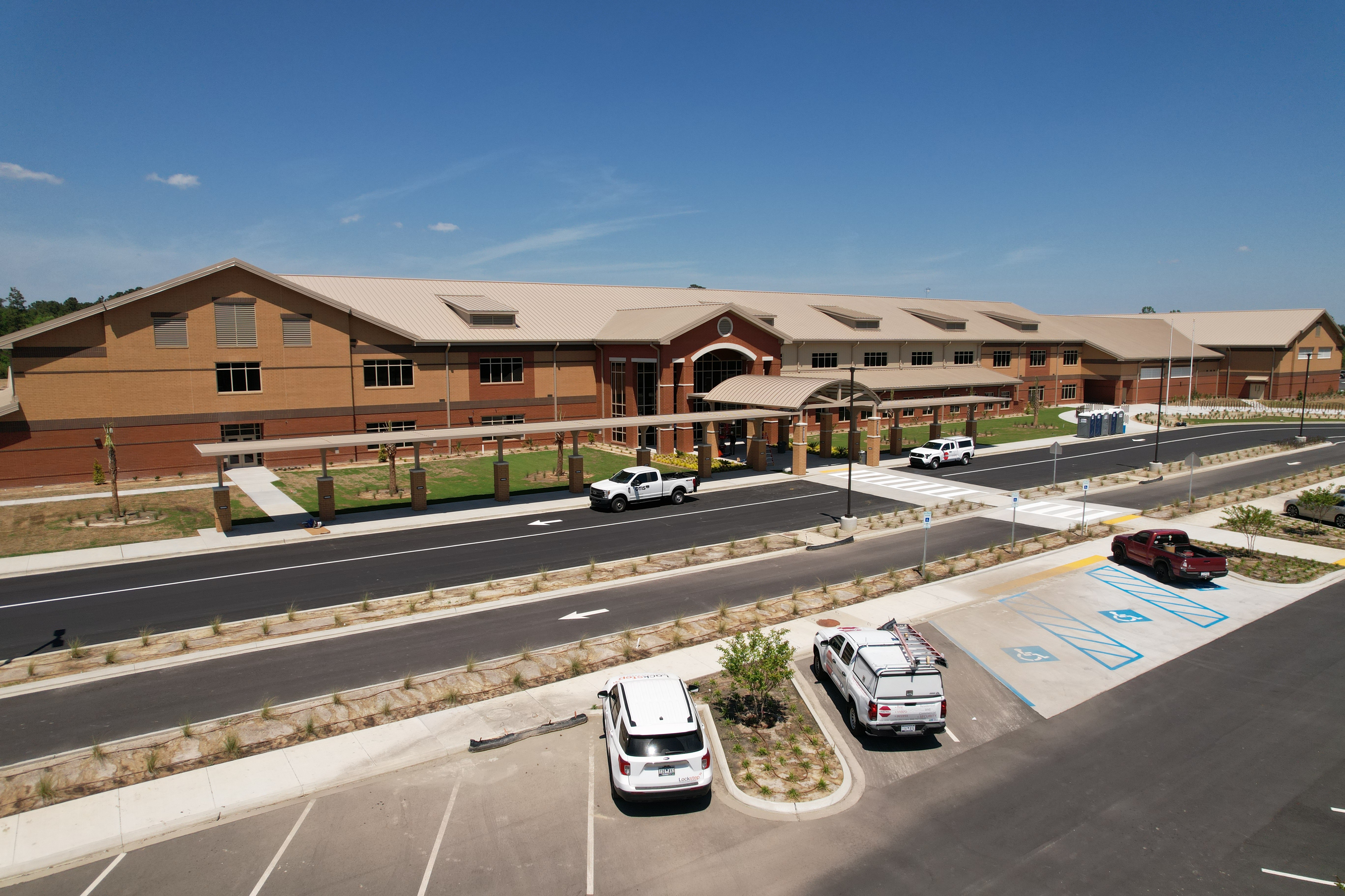 An aerial view of a parking lot with cars parked in it. A large building is in the background.