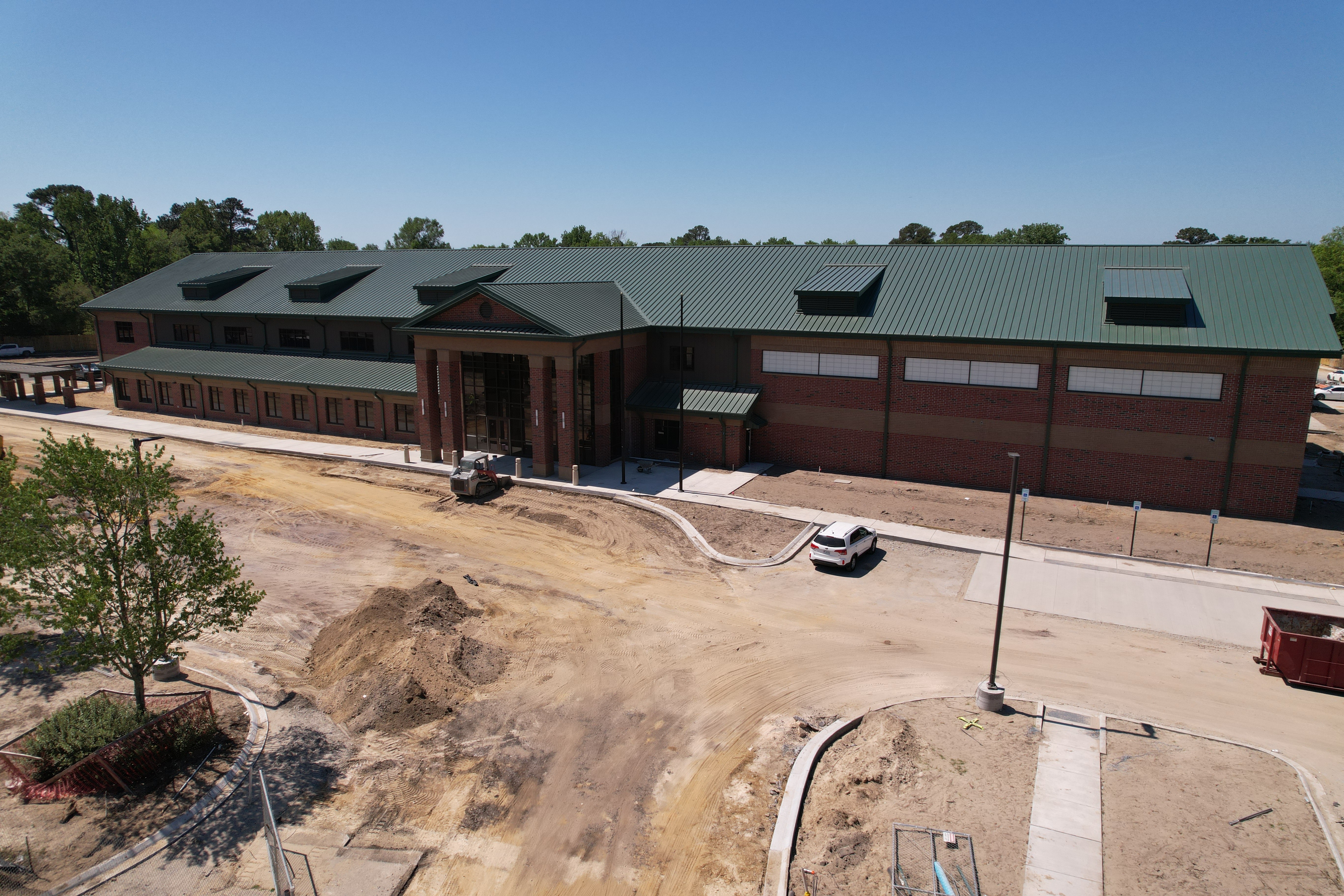 Building under construction with a green roof, a white car parked in front, and a dirt area.