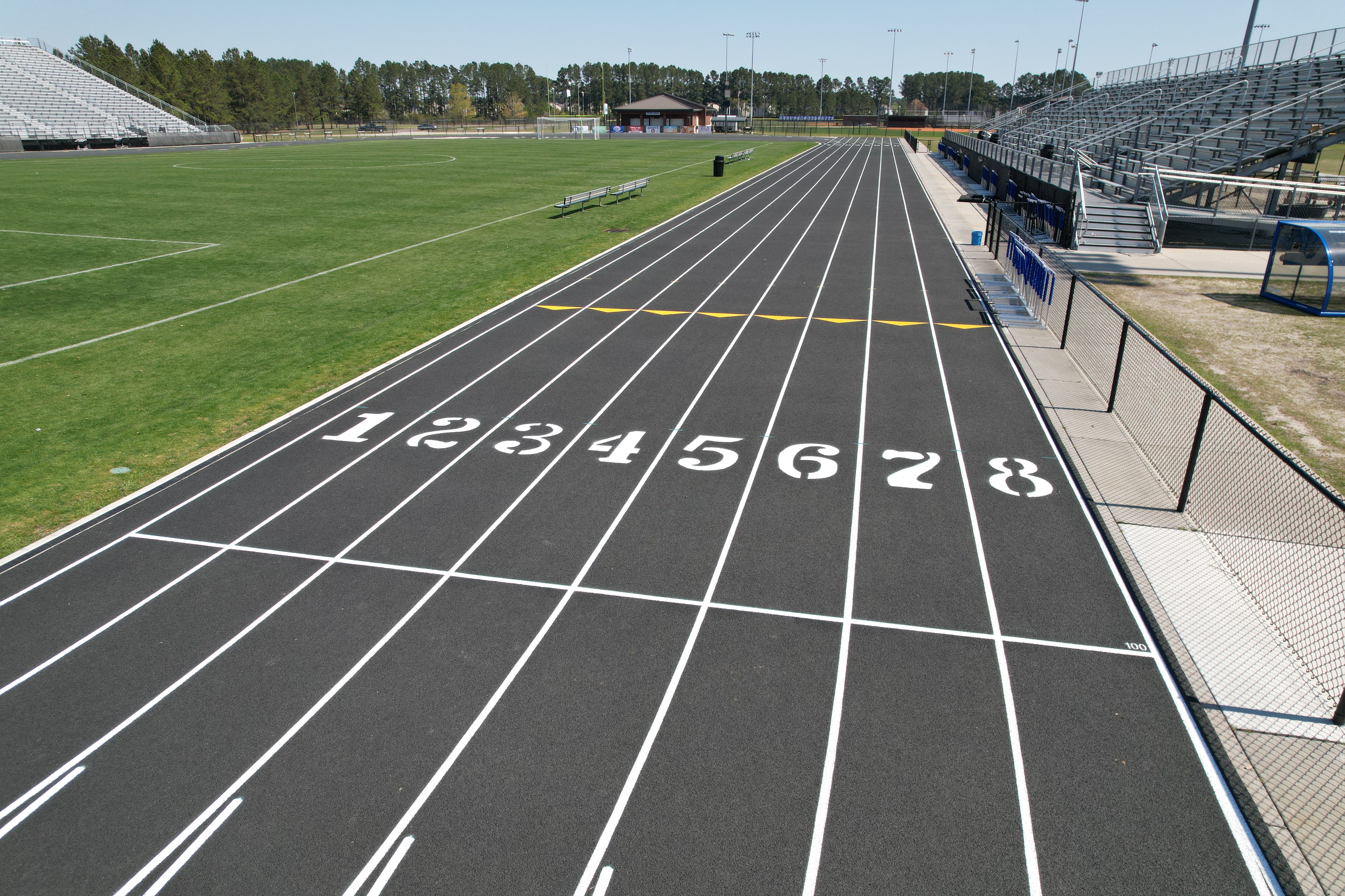 A running track with numbers 1-8 on lanes. The field is empty and surrounded by grass and bleachers.