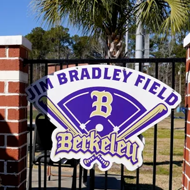 A person in a reflective vest walks past a brick wall. Behind them is a sign for Jim Bradley Field.