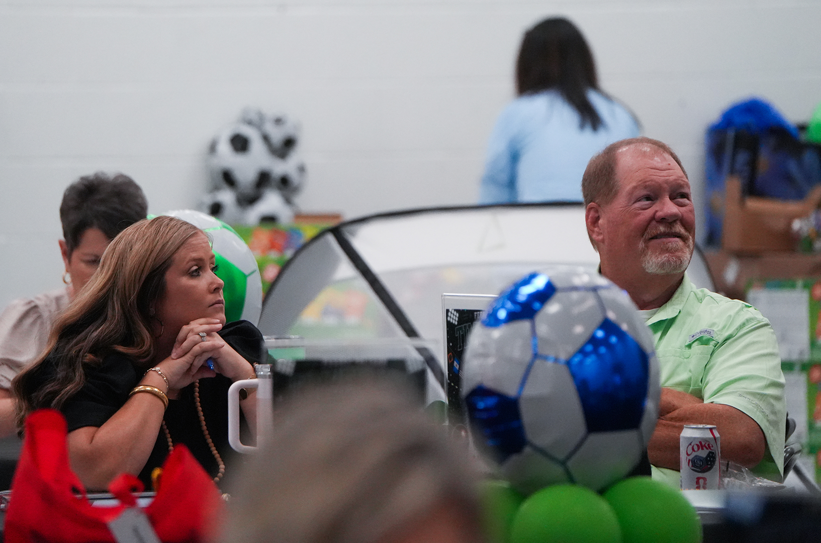 People at an event, including a man and a woman with a soccer ball and a can.