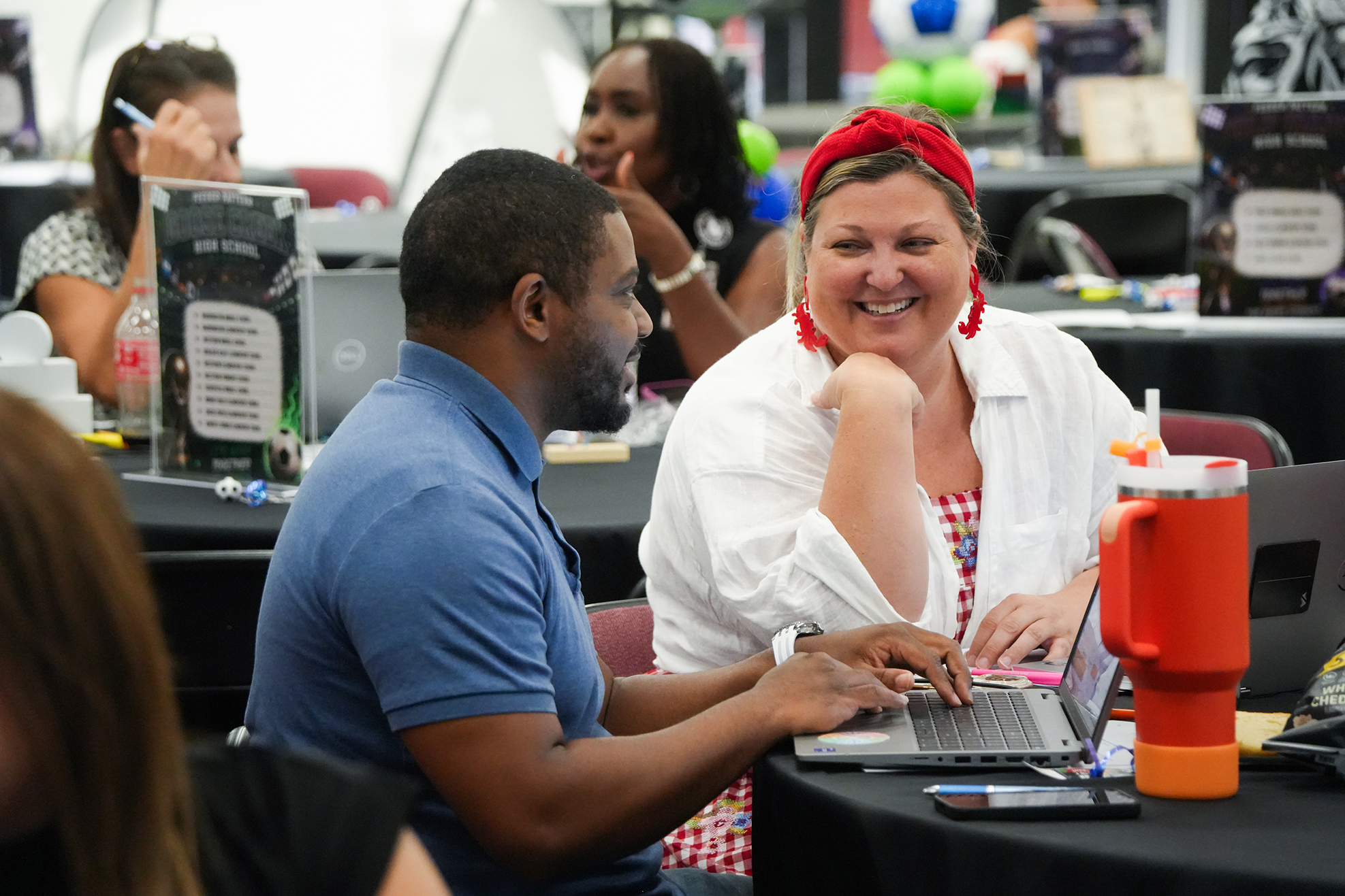 Man and woman sitting at a table with a laptop. The woman smiles, and the man appears to explain something.