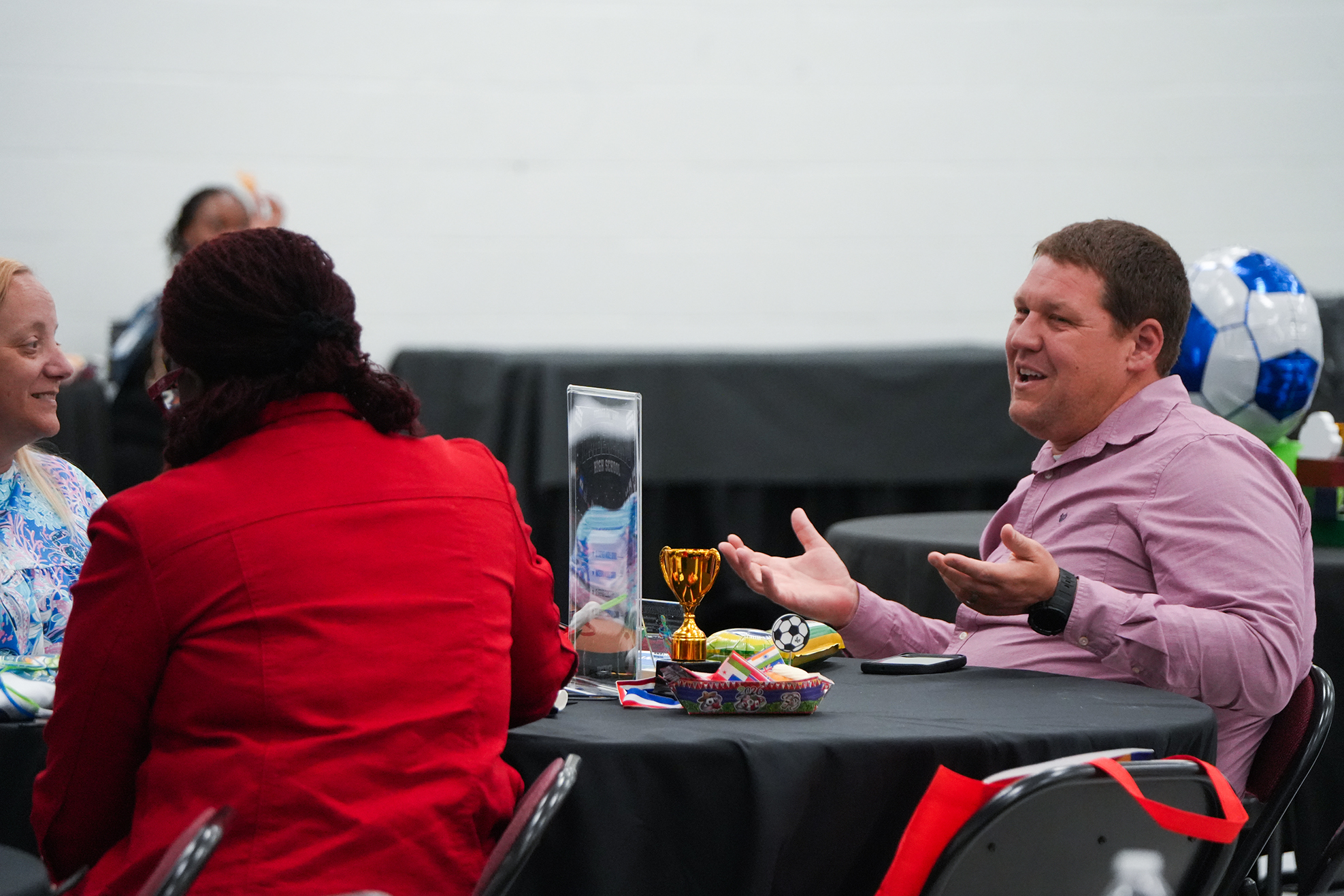 Three people at a table in a conference room. One person gestures with hands while another listens.