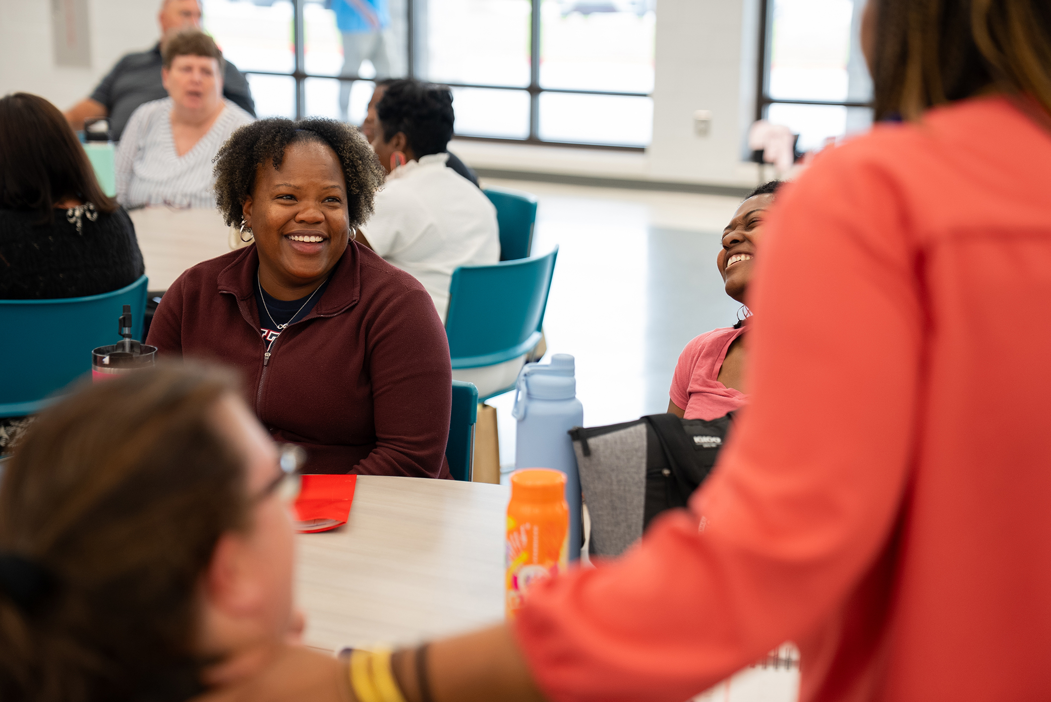 Several adults seated at a table, engaging in conversation. One woman smiles and looks toward another.