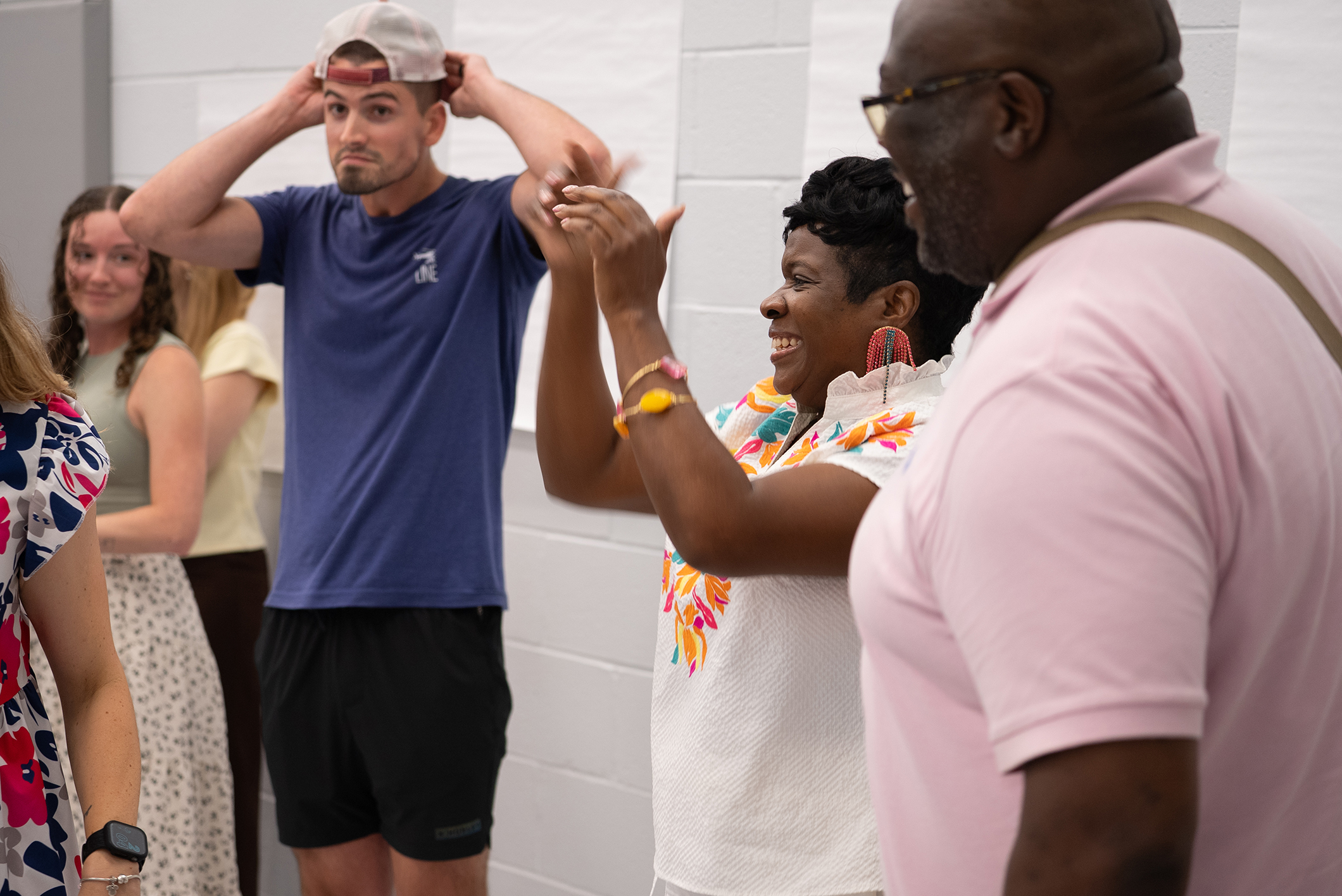 A group of people in a room; a man adjusts his hat while a woman holds his hair.
