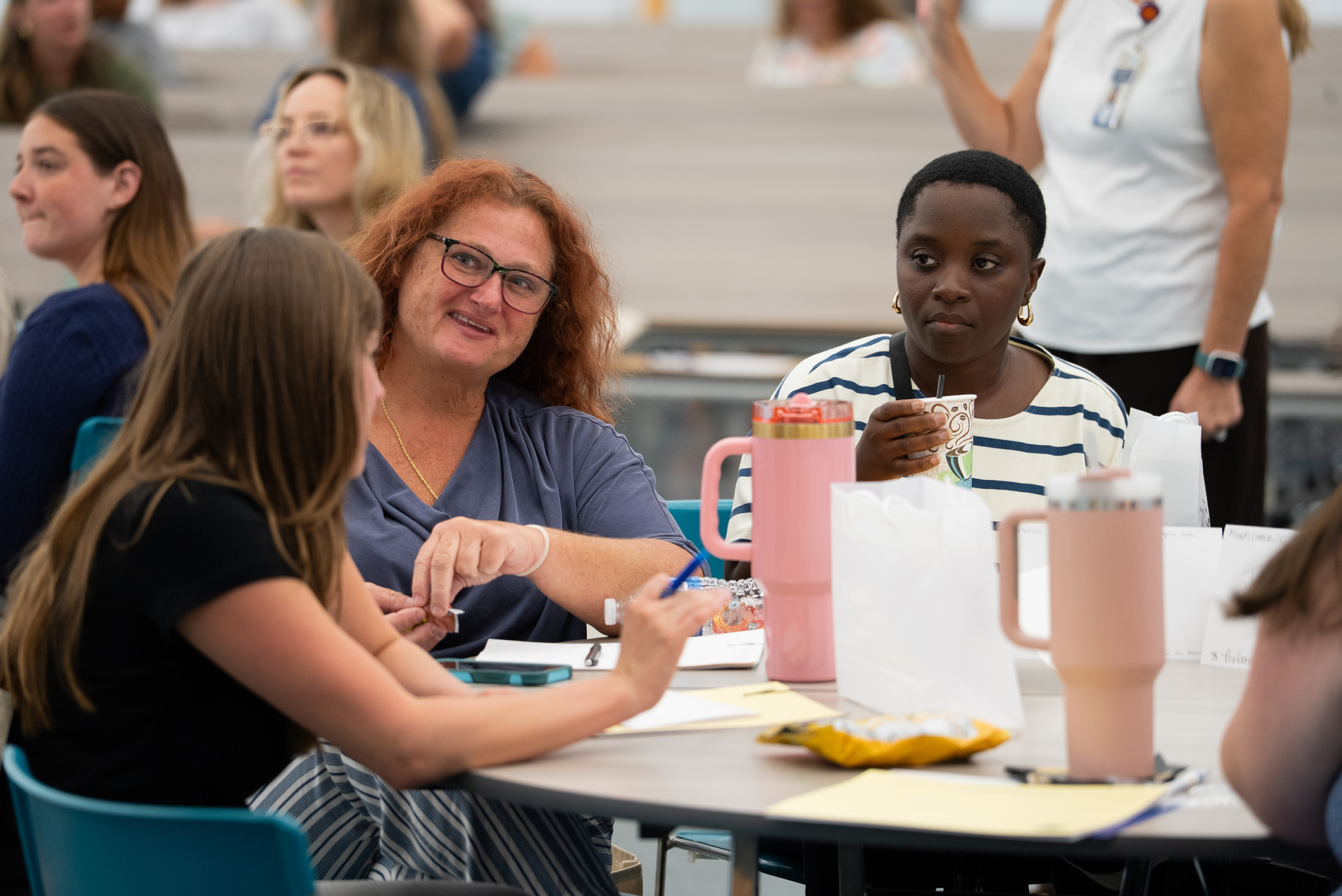 A group of people sit at a table in a classroom, facing each other and engaging in conversation.