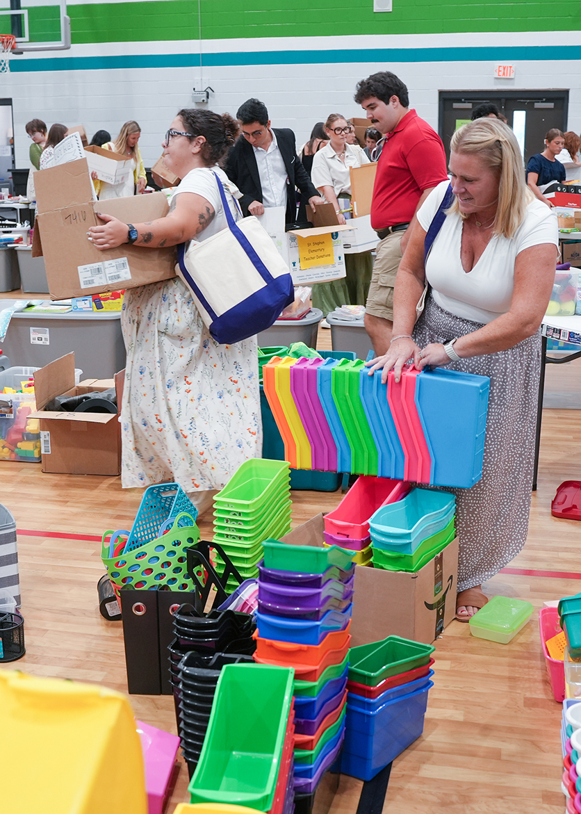 People in a room with storage bins. Two women hold bins, one holds a box. Other people are behind them.