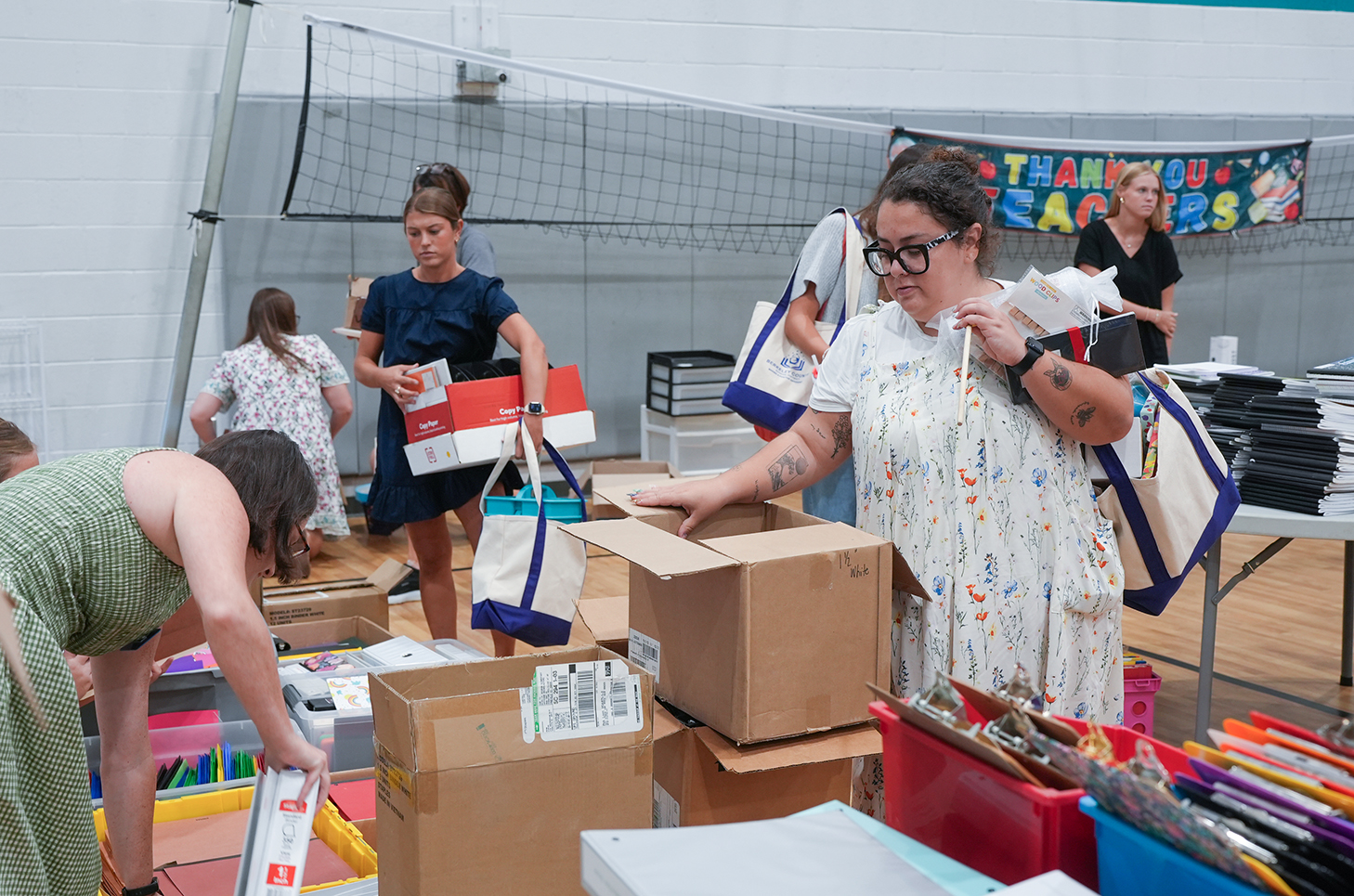 Several people sorting through boxes and bags inside a gymnasium with a volleyball net.