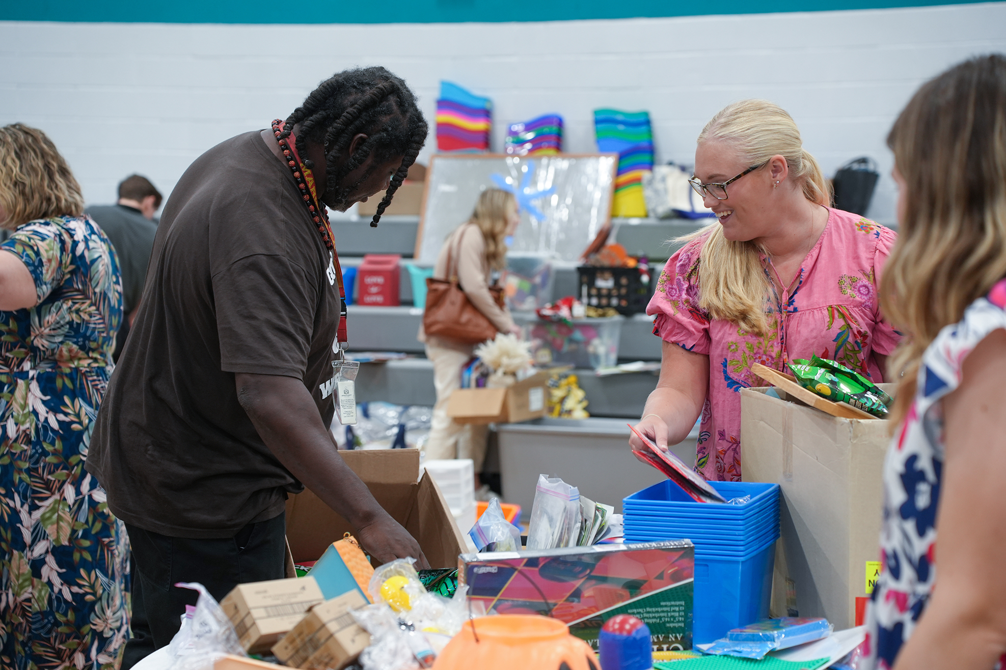 Individuals sort through and pack items into boxes in a room with shelves in the background.