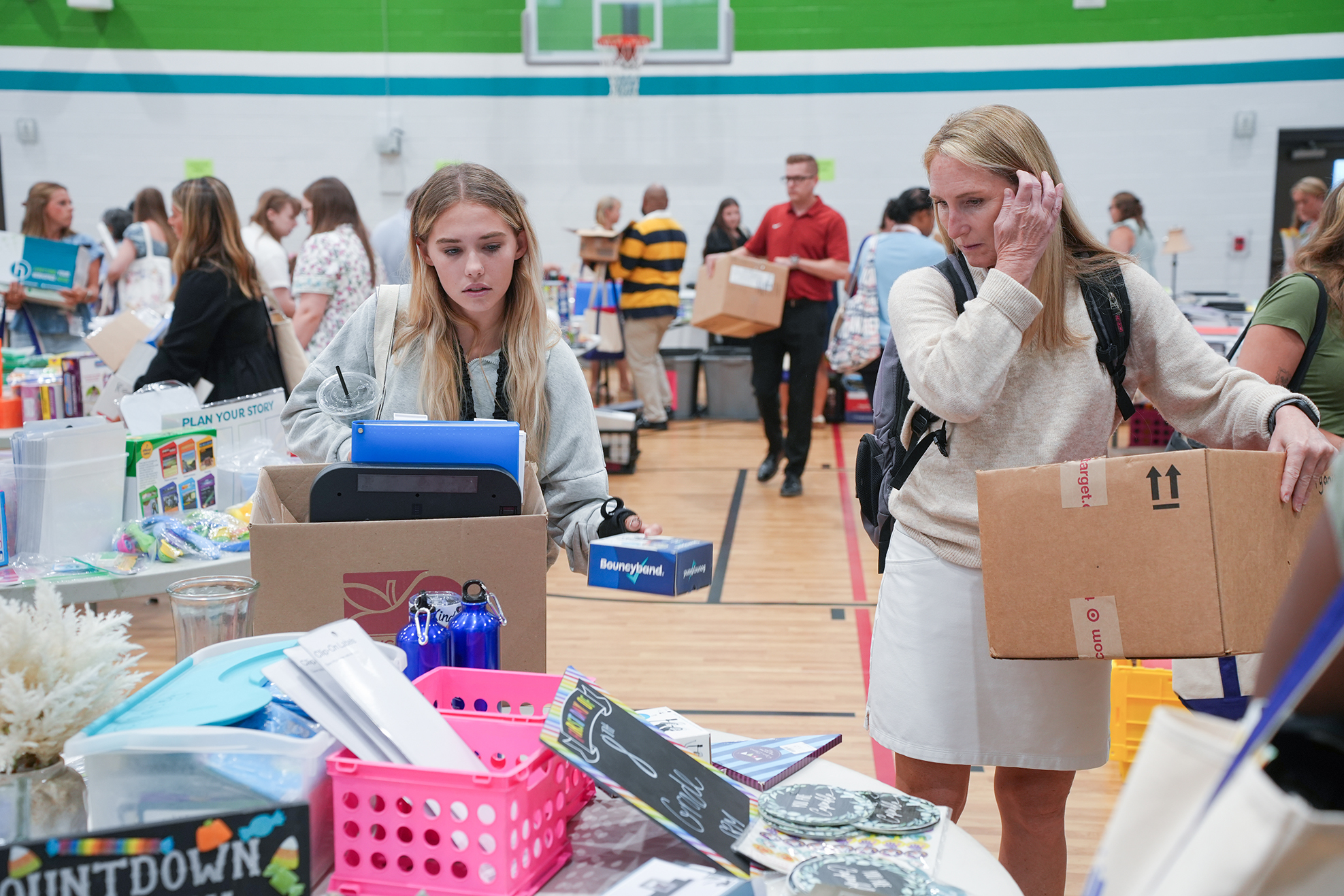 A room with people around tables. One person carries a box, while another browses in a box.
