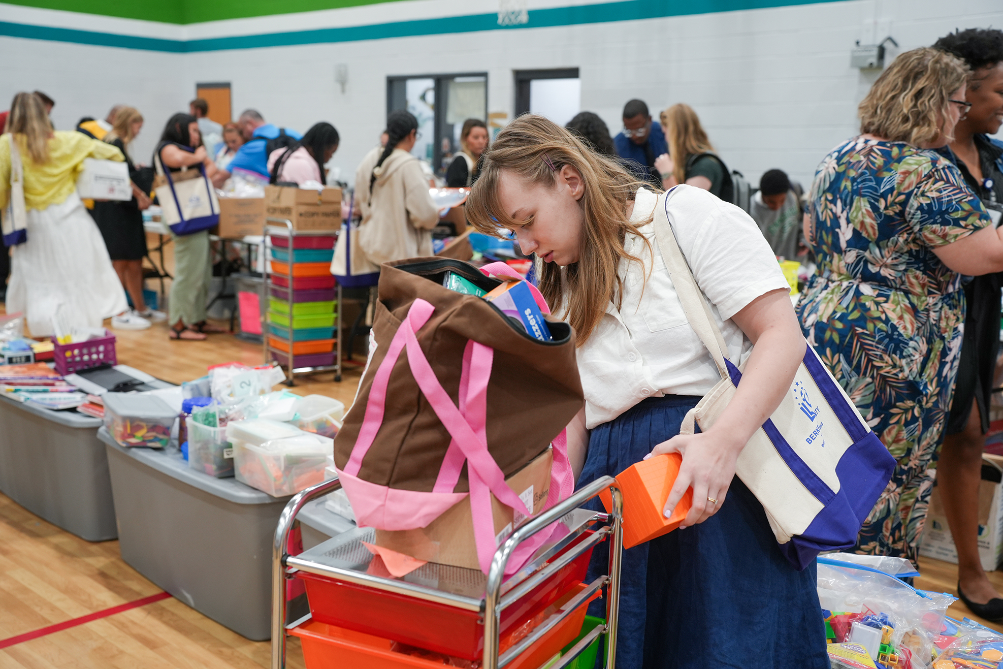 A woman examines items in a cart while surrounded by others at a community event.
