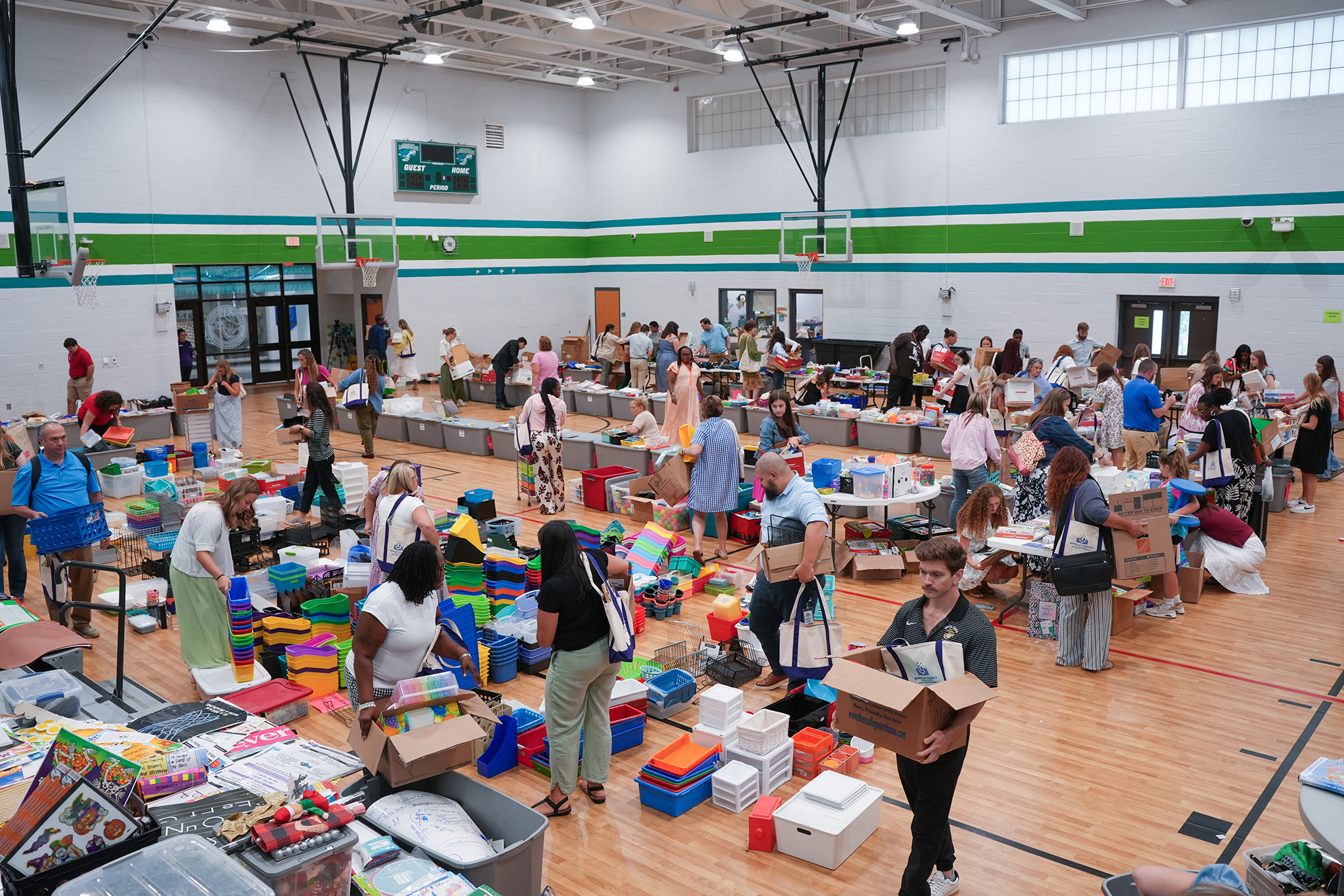 A crowded gym with many people walking around. Tables are filled with items like toys and boxes.