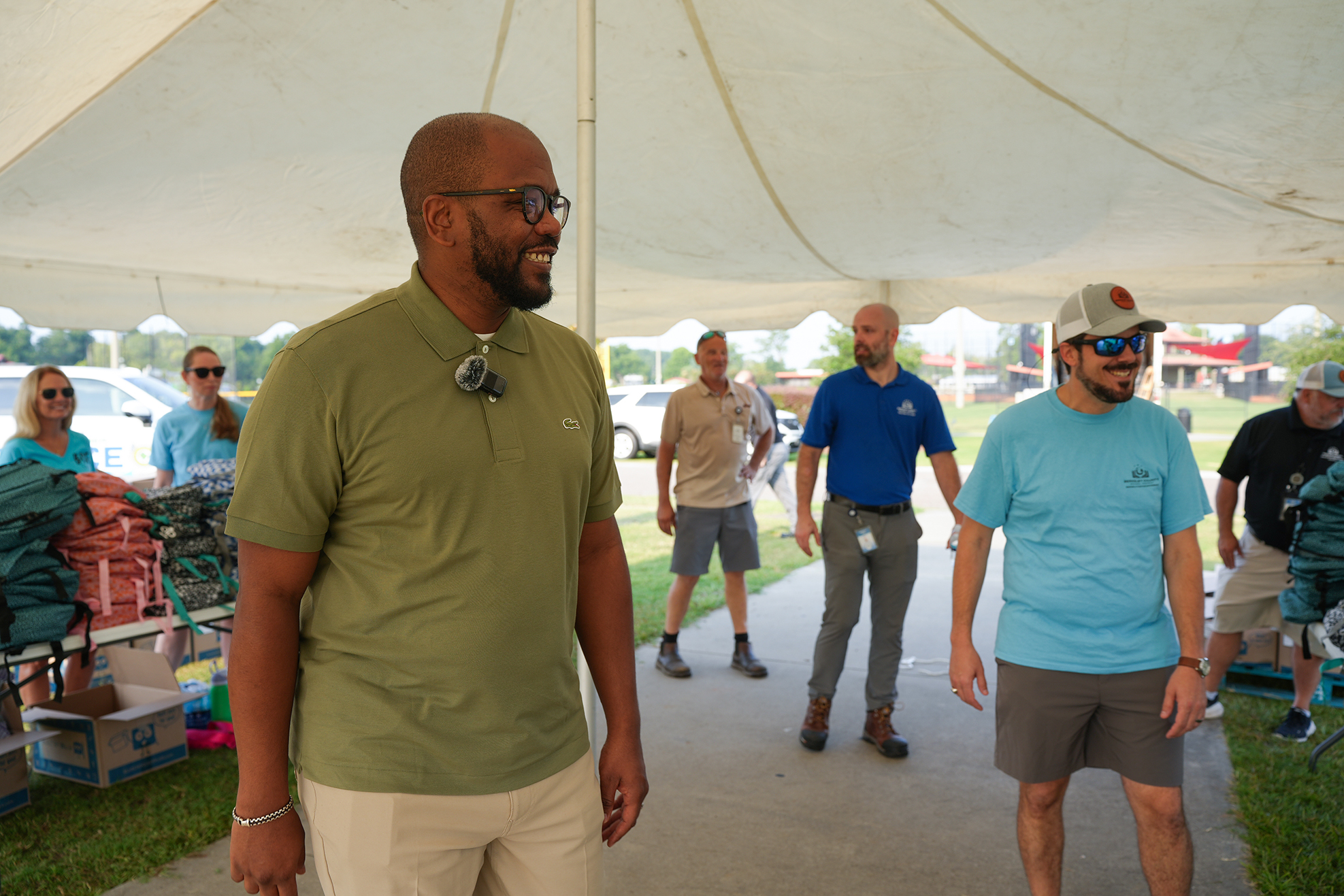 A group of people walking under a tent. One man wears glasses and a green polo shirt.