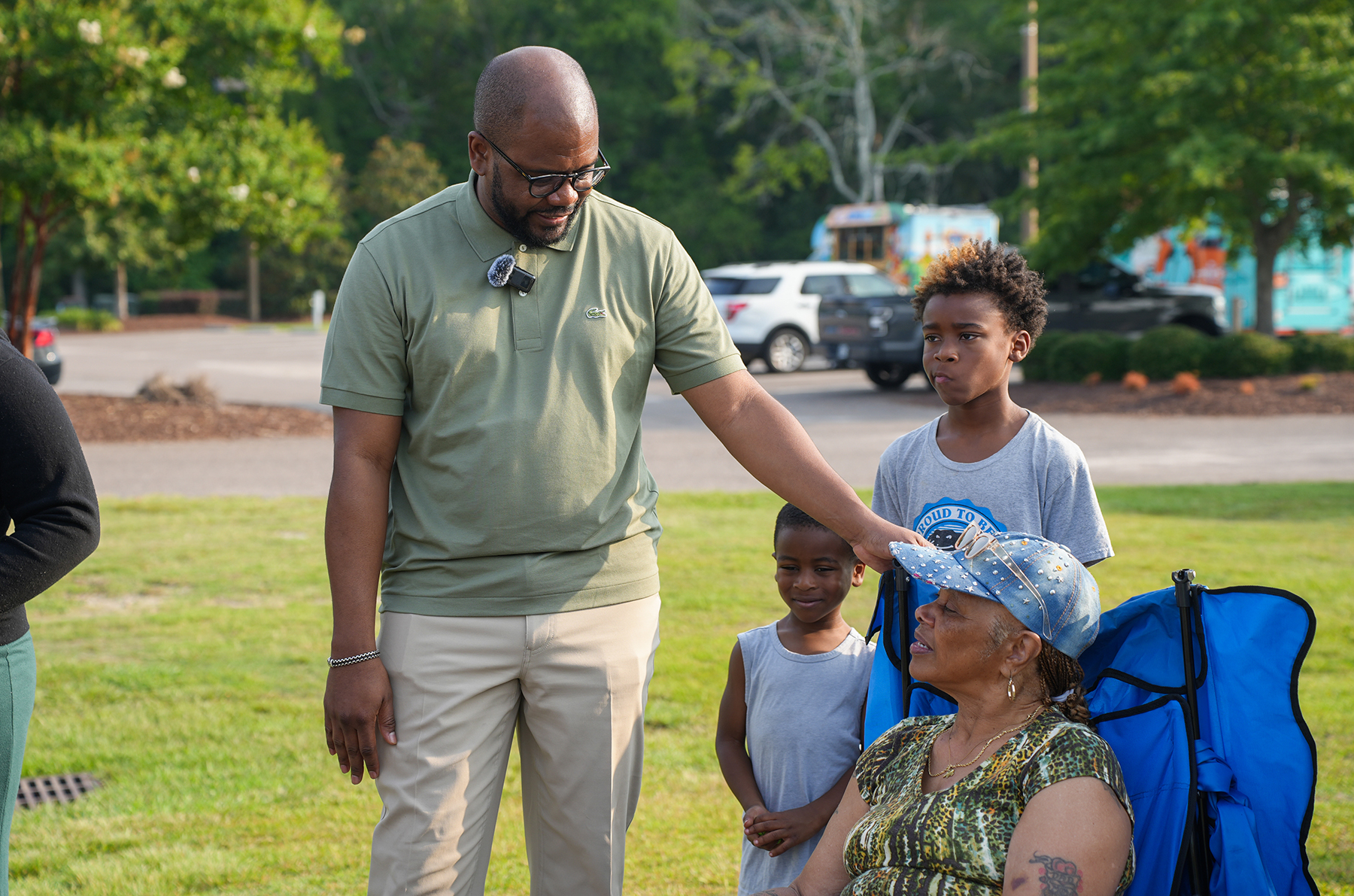 An adult man adjusts the hat of a seated woman. Two children stand behind them, one wearing a blue hat.