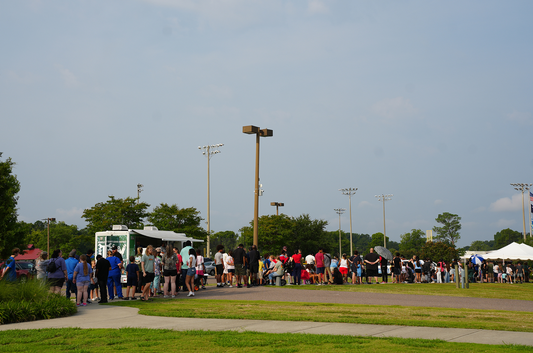 People stand in line outside under a clear sky; street lights and trees surround the area.