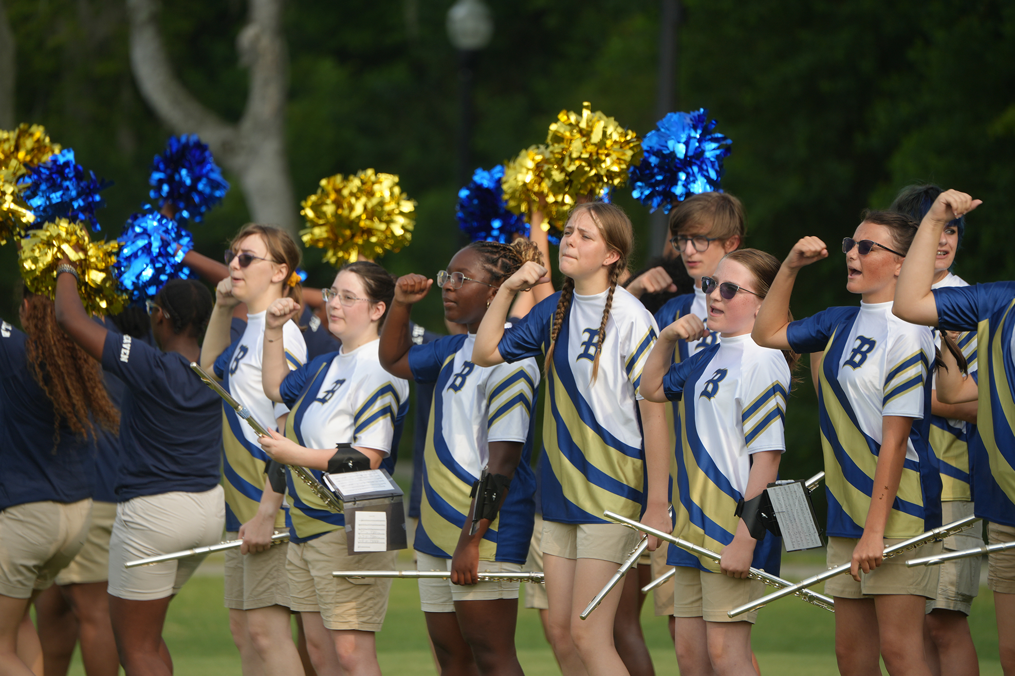 Group of cheerleaders on a field, holding pom-poms and batons, wearing blue and gold uniforms.