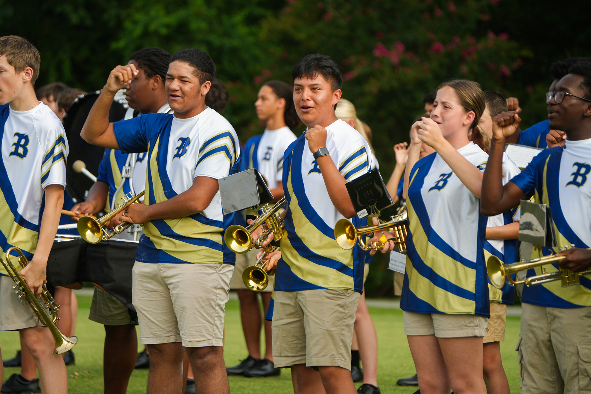 A group of students in matching blue and yellow uniforms stand outdoors, holding musical instruments.