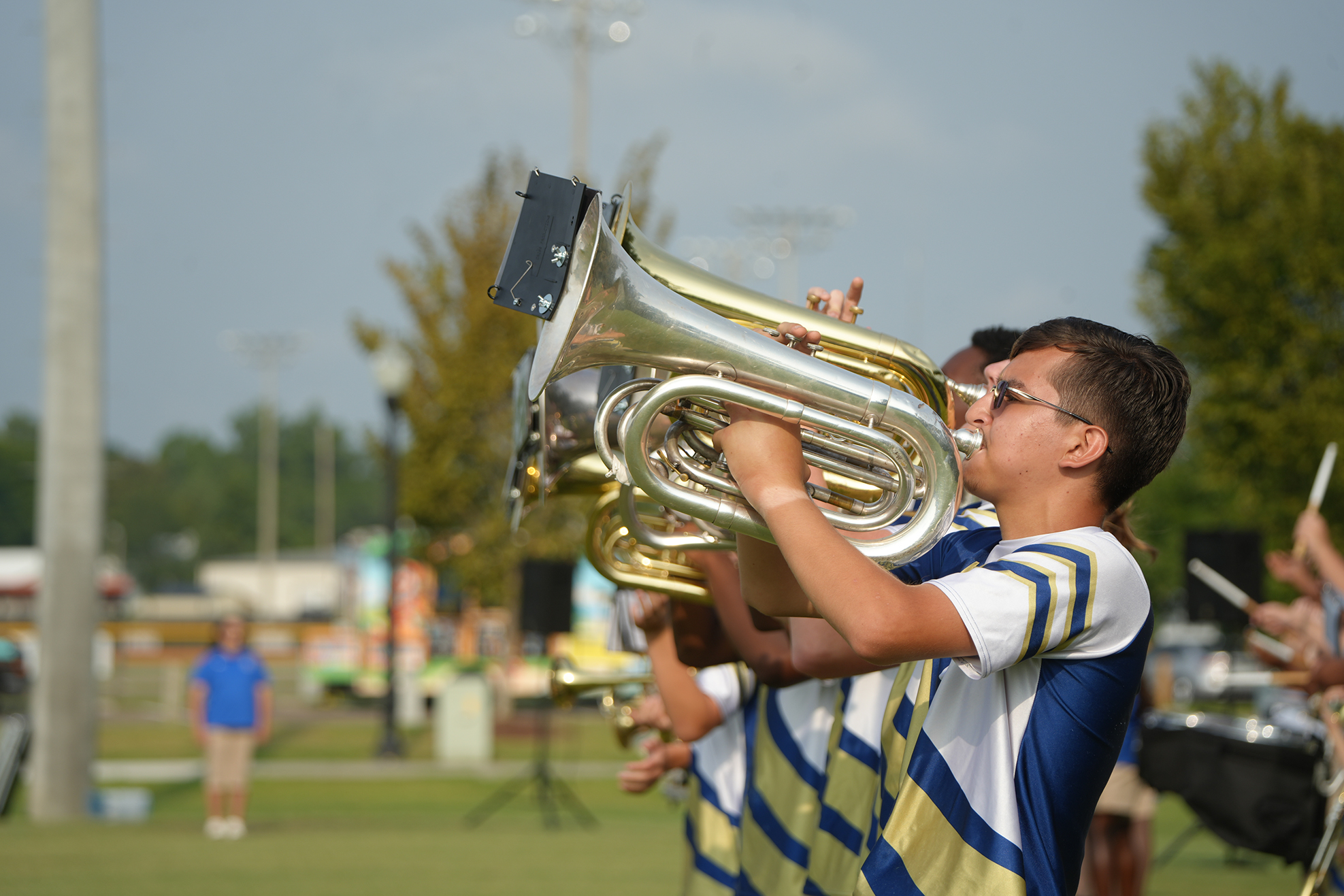 A young man plays a brass instrument in a marching band during an outdoor performance.