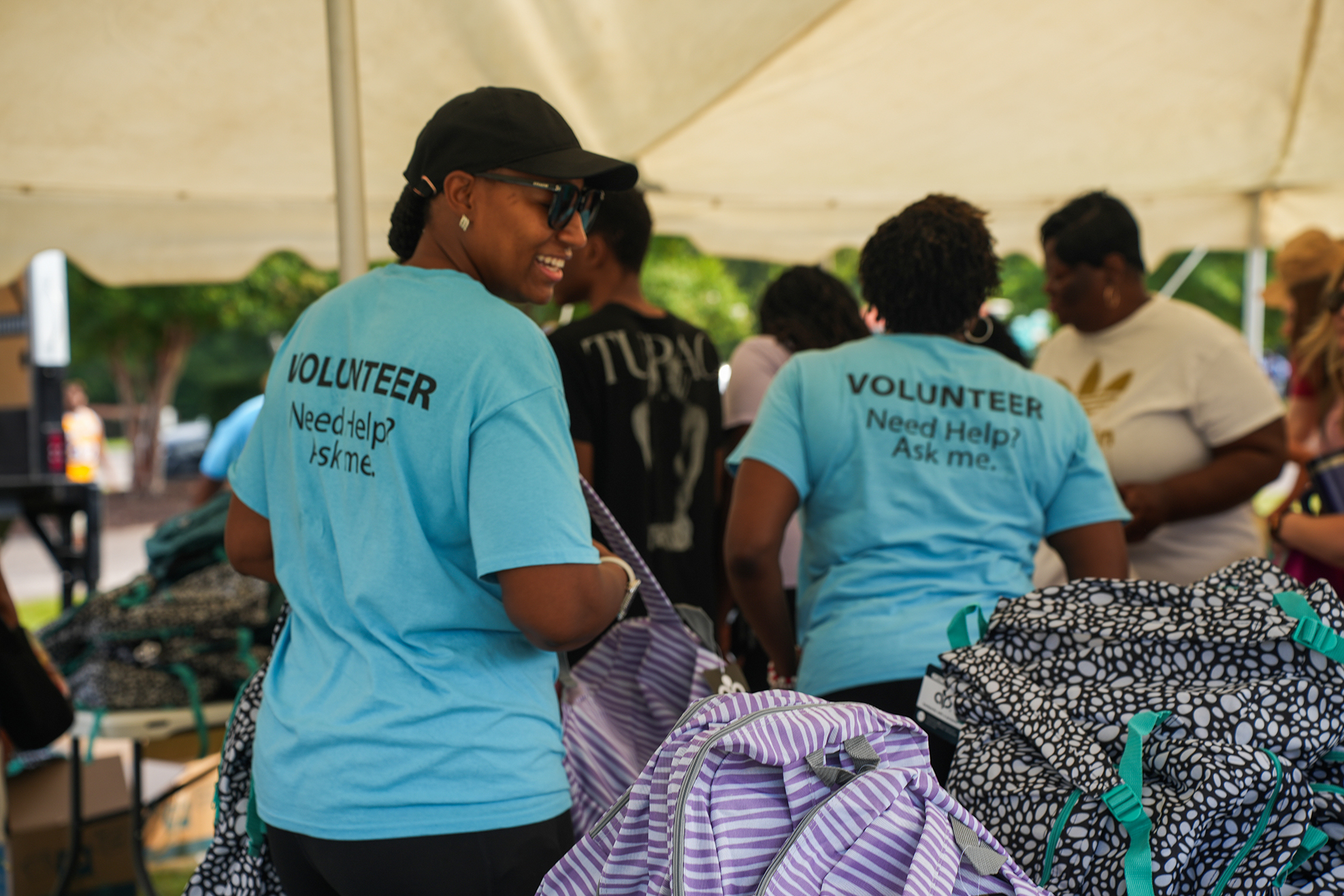 A group of volunteers, each with "Volunteer" shirts, stand under a tent with backpacks and bags around them.