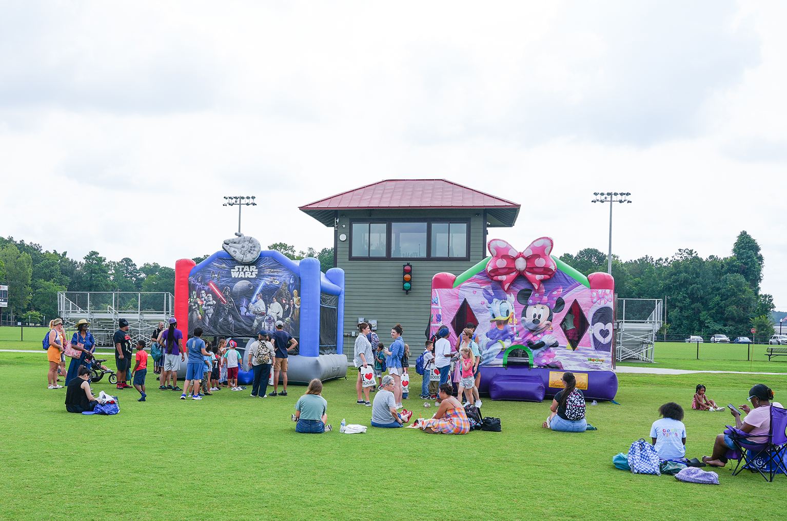 A group of people gather on a grassy field with inflatable attractions and a small building in the background.
