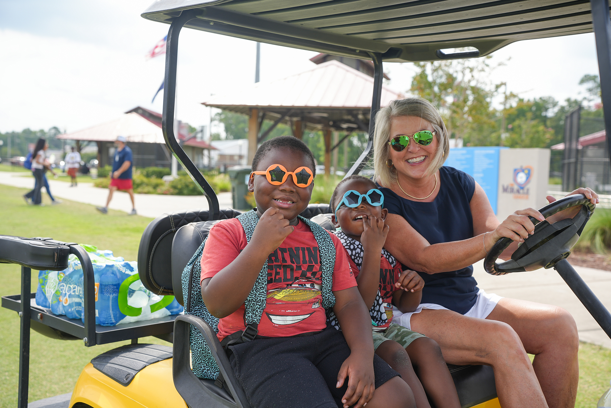 A woman and two children sit in a golf cart. The woman drives, and the children wear sunglasses.