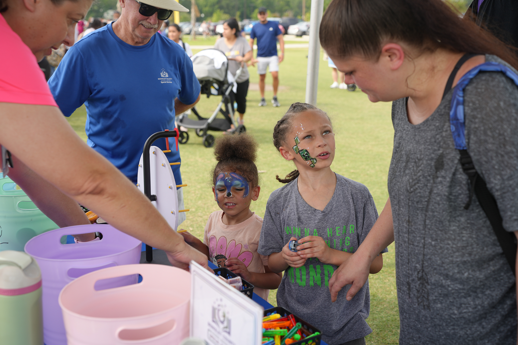 Two girls and an adult at an outdoor event. One girl has blue face paint, another has brown hair.