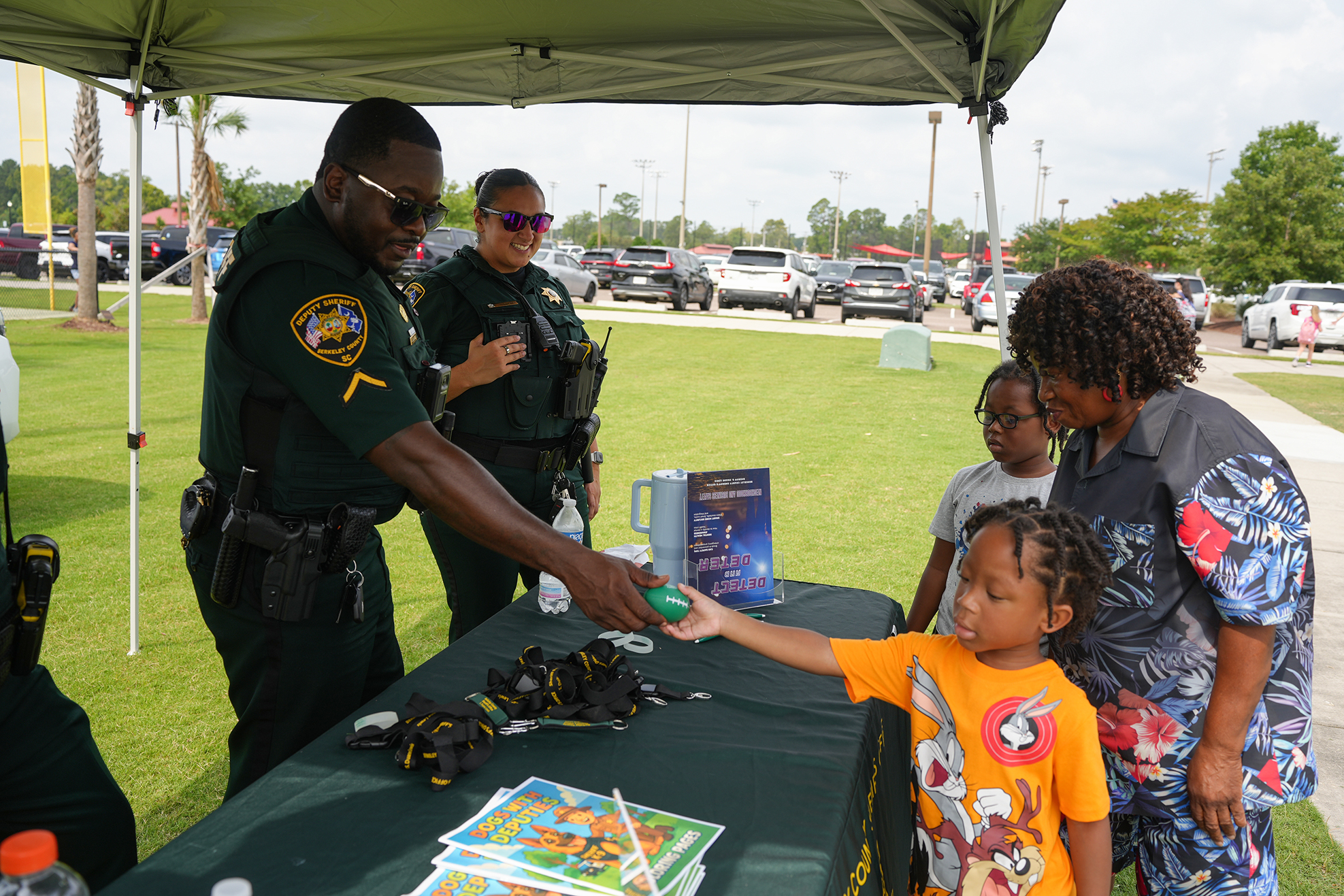 Police officers at an outdoor event; one hands a small toy to a child in an orange shirt.
