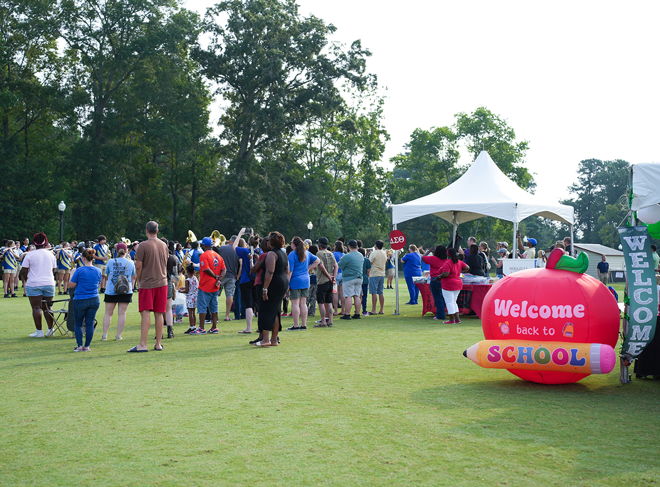 A grassy field with a large inflatable apple, a stop sign, and a tent. People gather and walk.