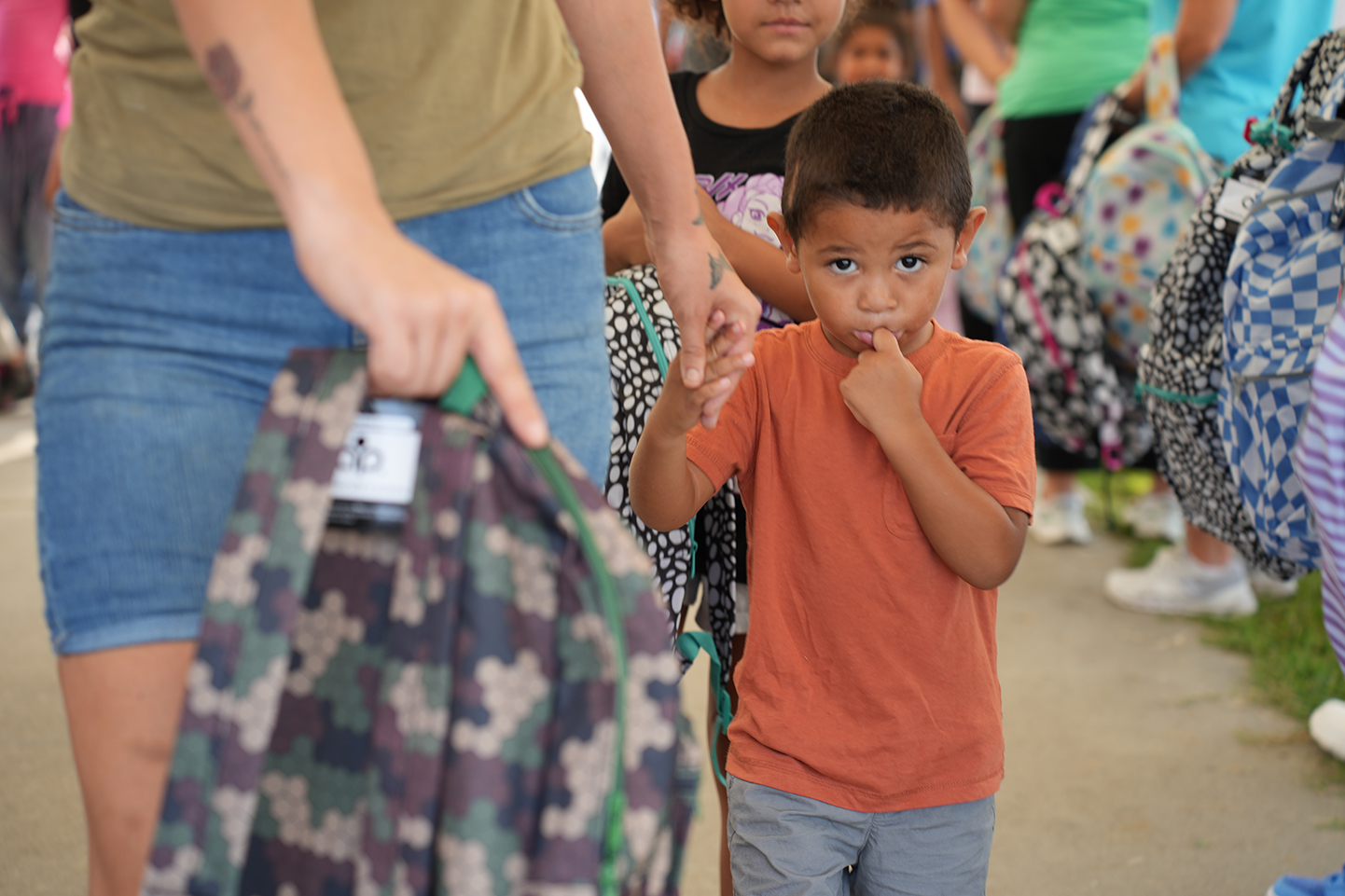 An adult holds a backpack while walking with a young boy with a worried expression.