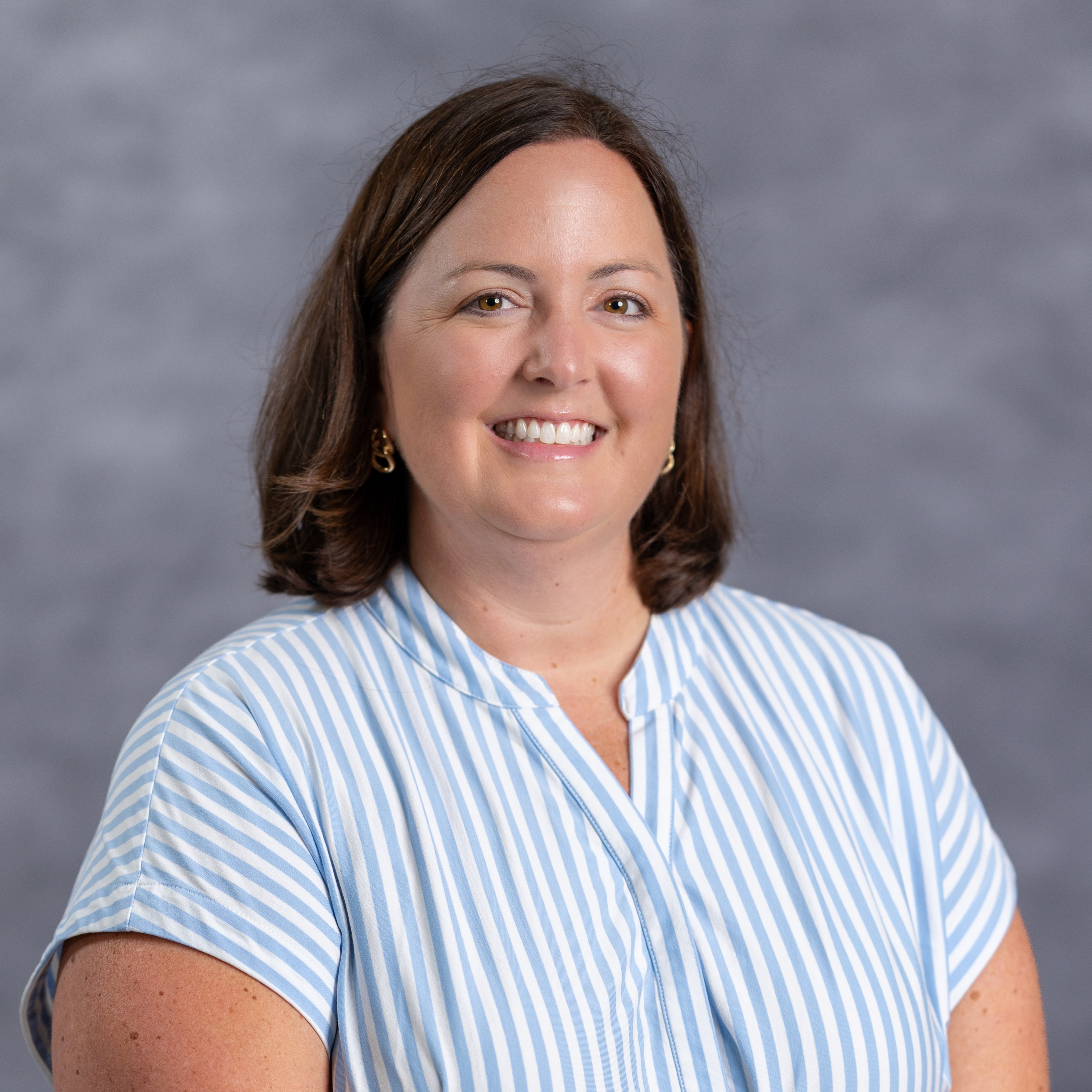 Woman in blue and white striped shirt with short brown hair, smiling at camera.
