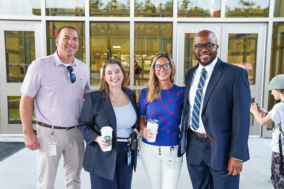 Four adults stand close together in front of a building entrance. Two men and two women.