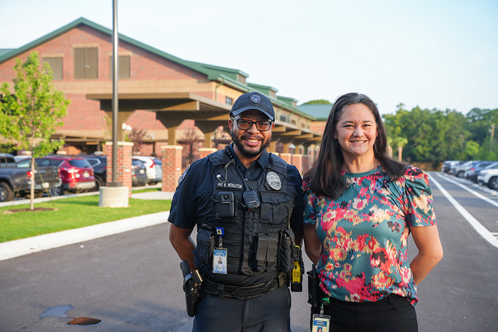 A police officer and a woman stand in front of a building. They smile and appear to be posing for a photo.