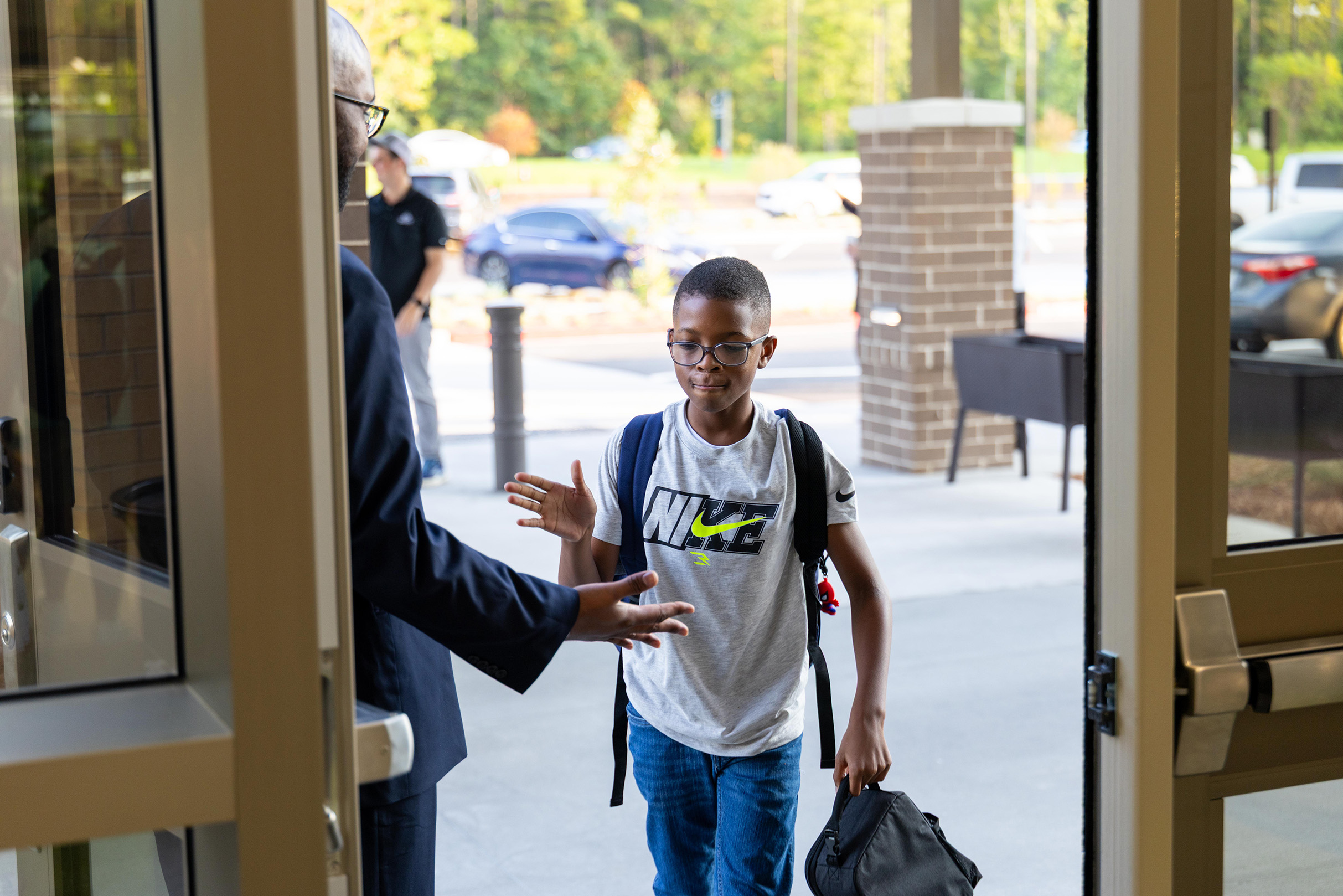 A man and a boy with glasses and a backpack are exiting a building with an open door.