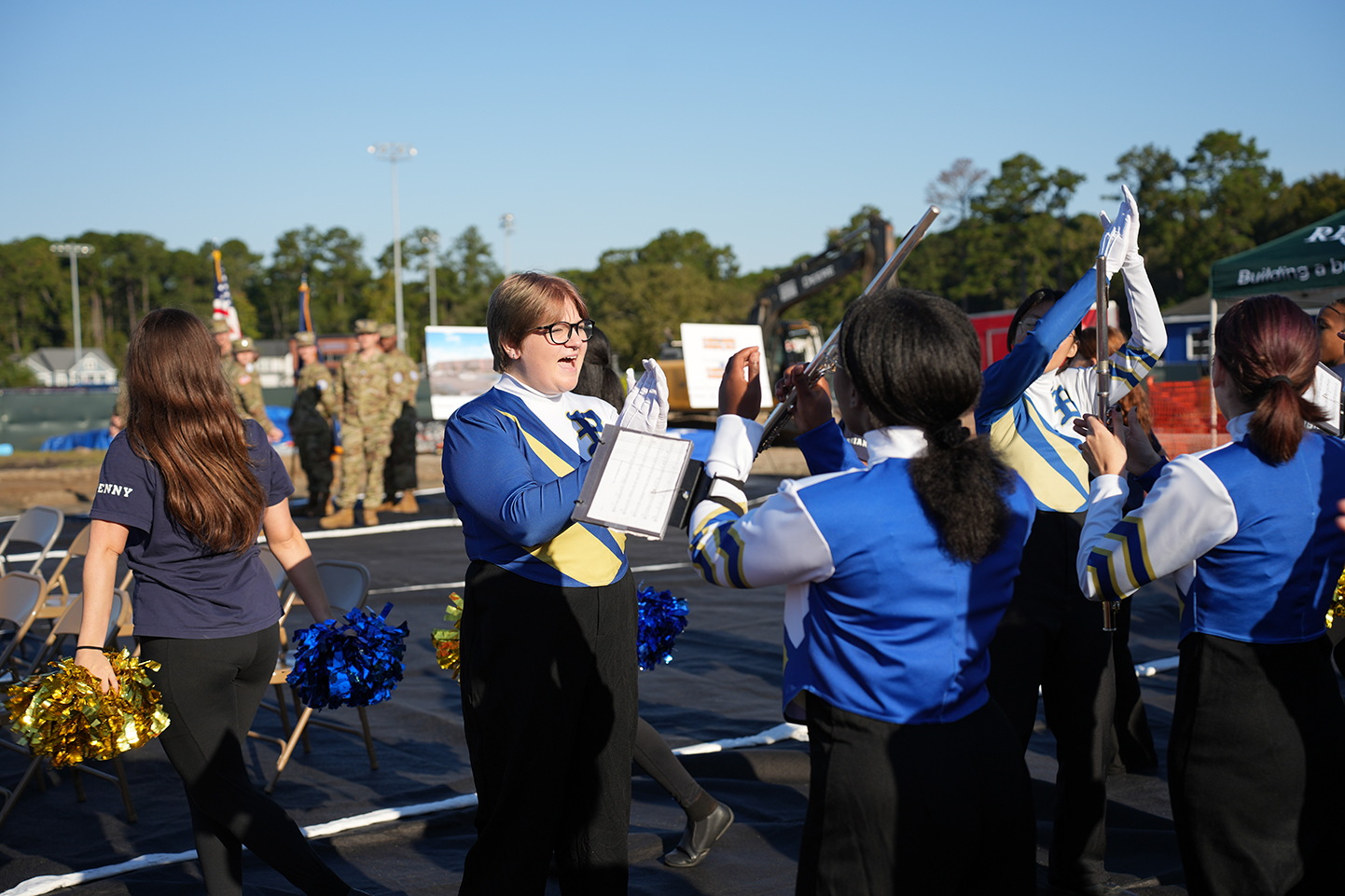 Six individuals in blue and white uniforms stand on a road, one holding a flag, another a book.