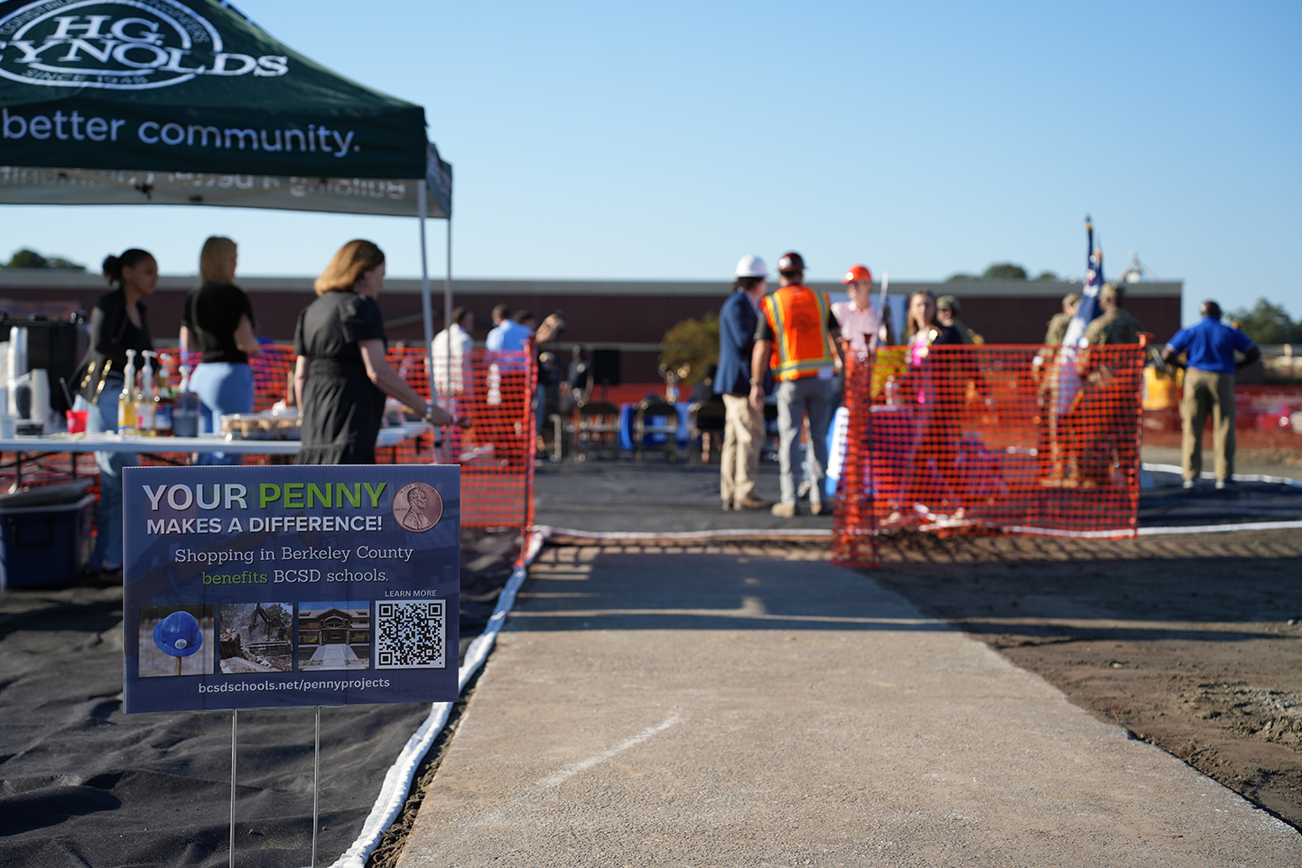 People at a school construction site; tent, barrier, sign on sidewalk.
