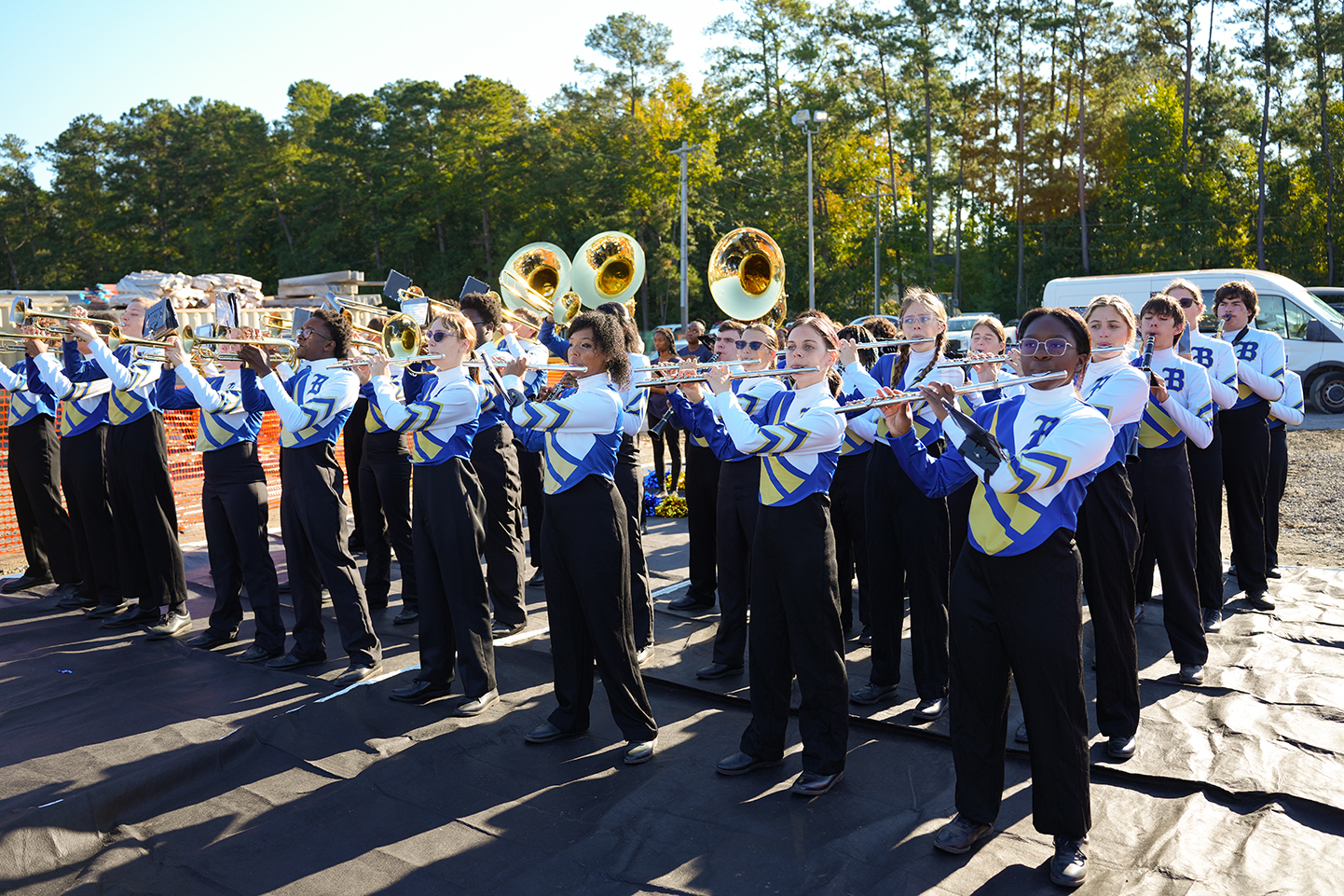 A marching band on a black surface, playing instruments, with trees in the background.