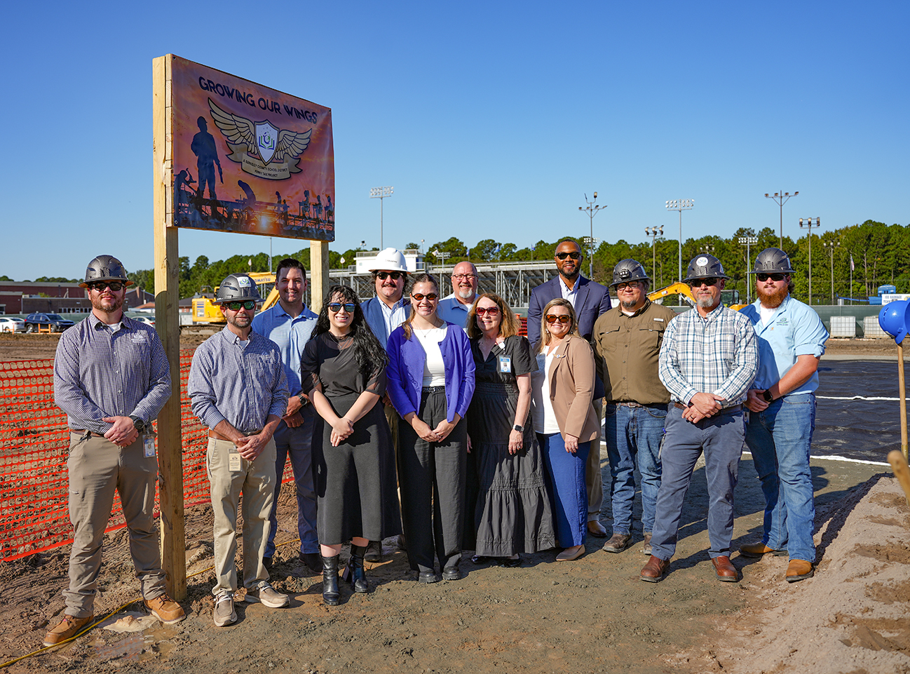 Group of people in construction gear posing for a photo in front of a new sign.