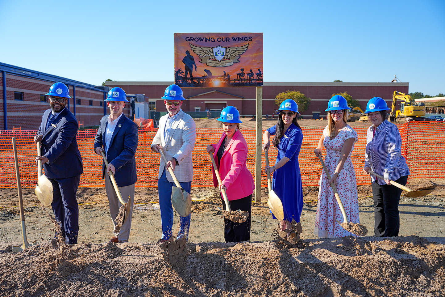 A group of people holding shovels at a construction site with a sign in the background.
